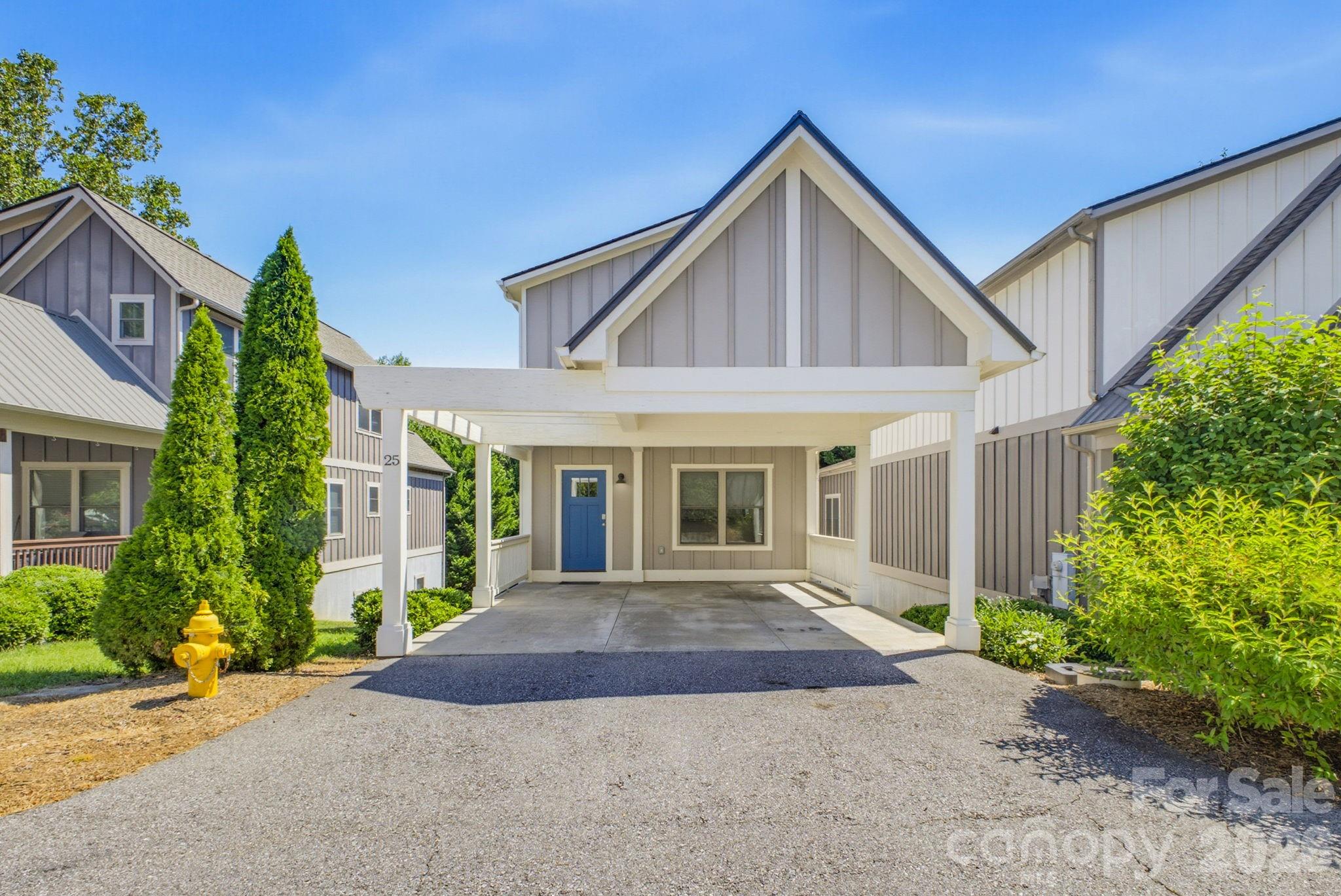 Gray-and-white home with a covered carport, blue front door, and landscaped entrance.