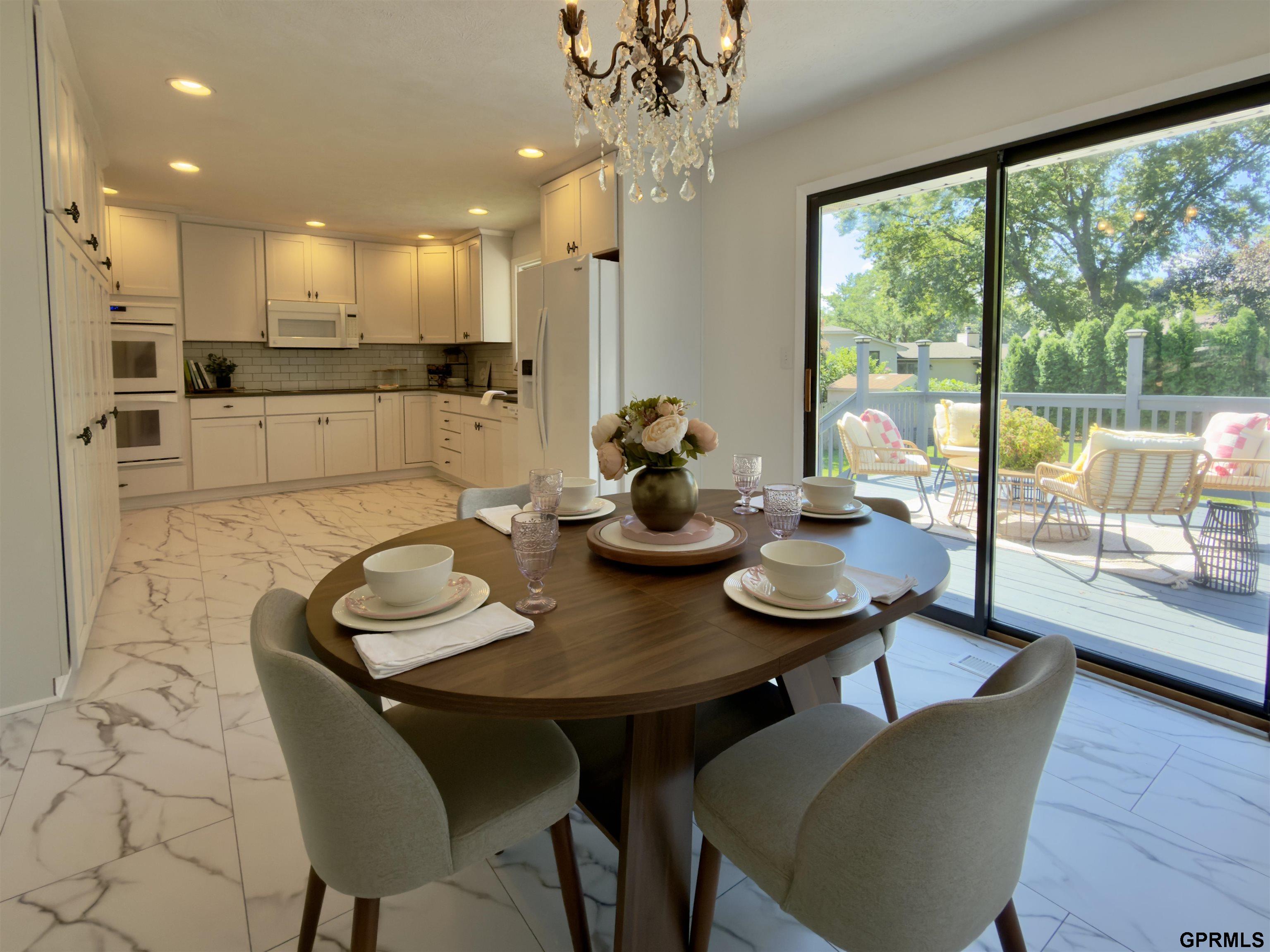 Dining area beside a white kitchen, with a set table and sliding doors to a sunny deck.