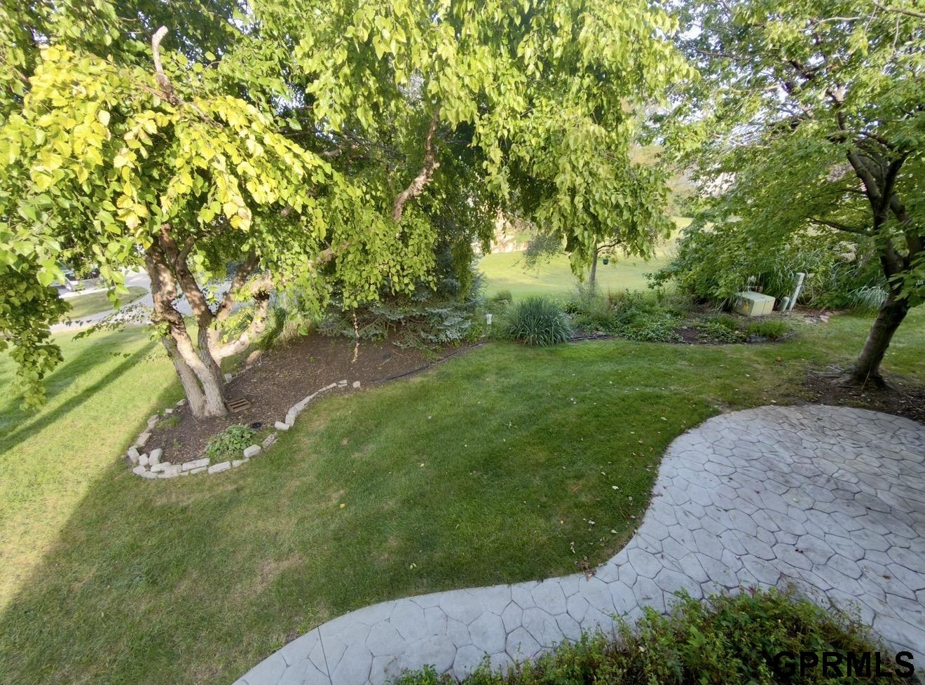 Landscaped backyard with mature trees, garden beds, and a curved paved patio.