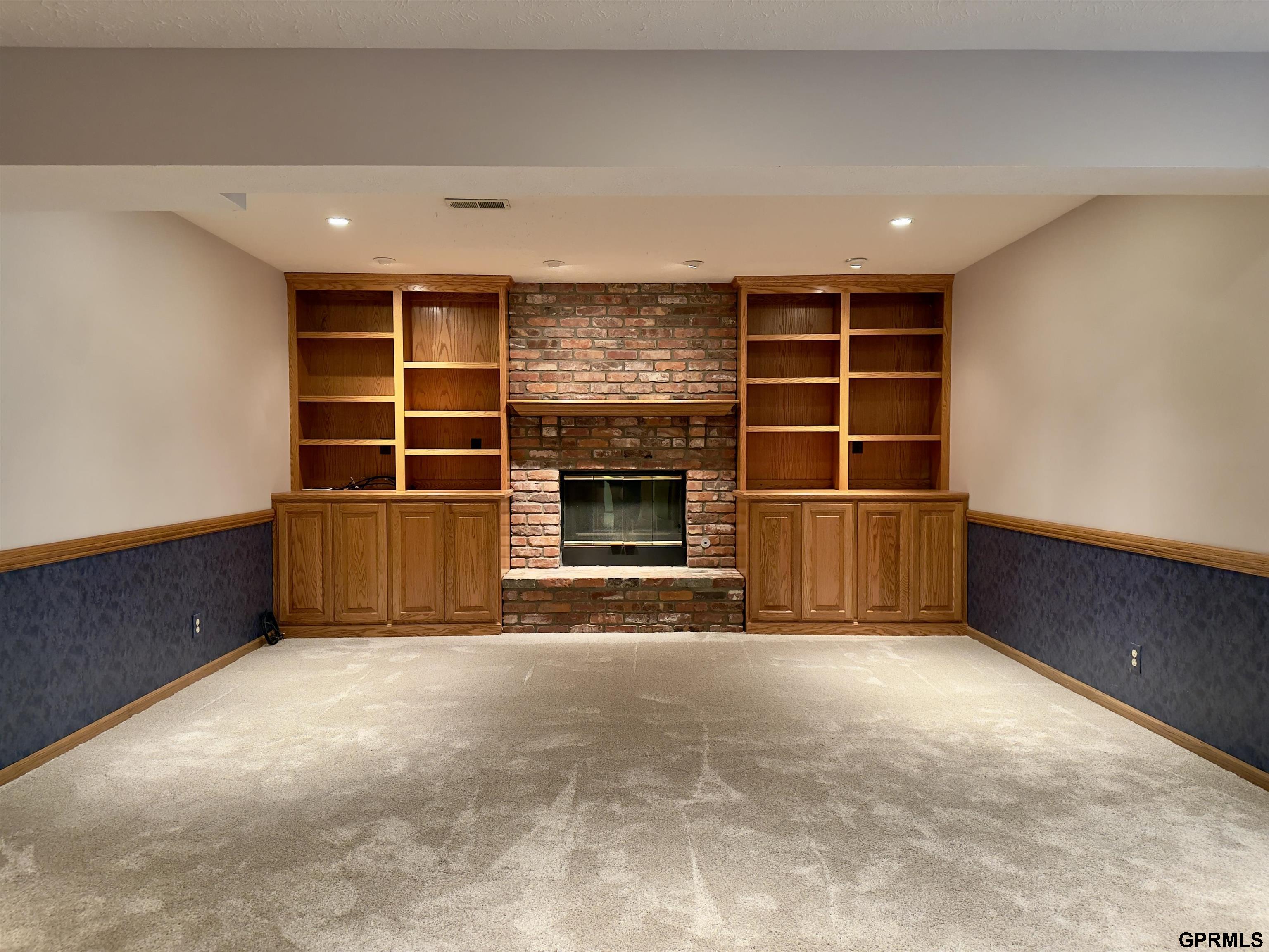 Living area with a brick fireplace and built-in wooden bookshelves and cabinets.