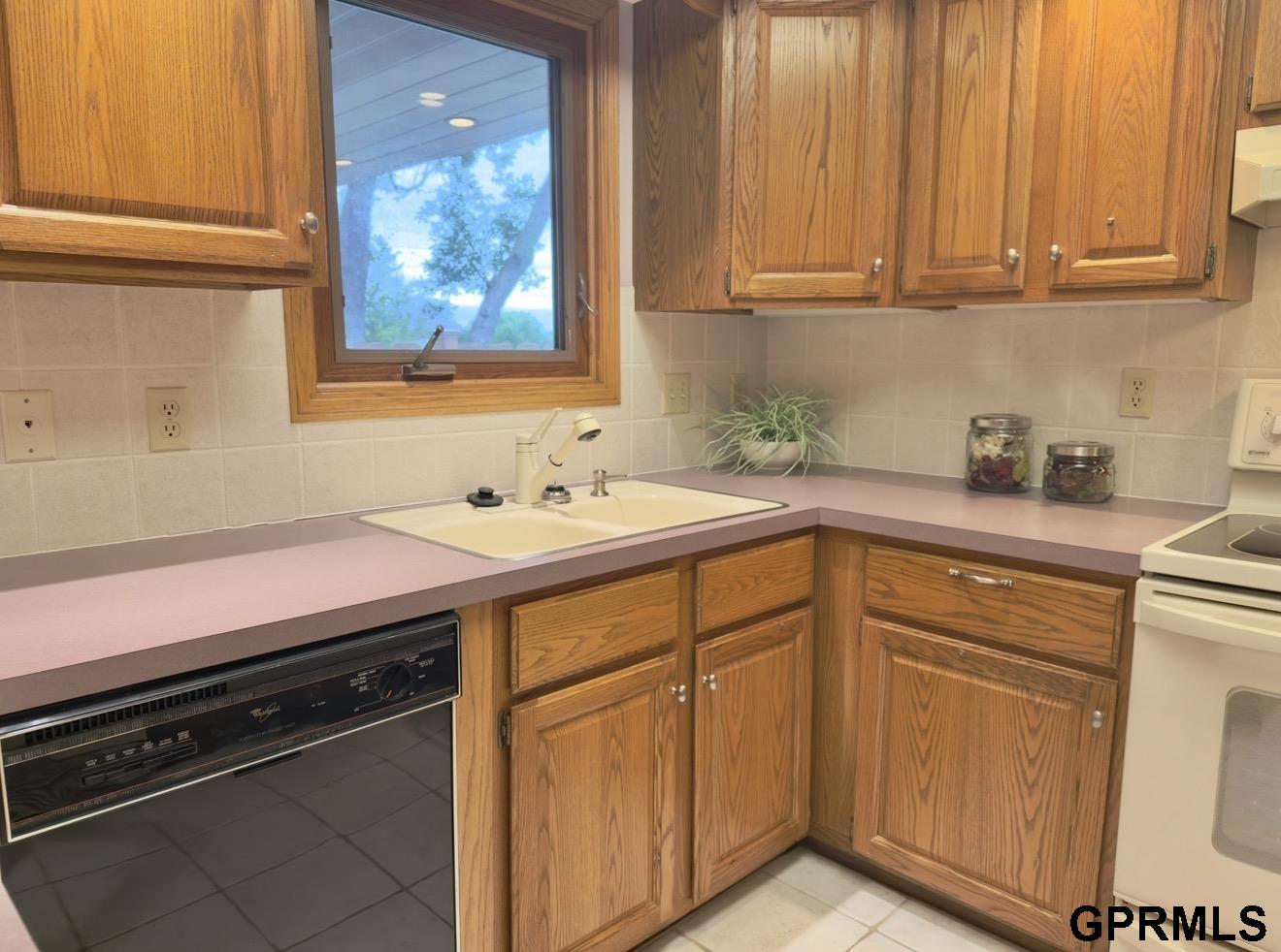 Kitchen with wood cabinets, pink countertops, a window above the sink, and a built-in dishwasher.