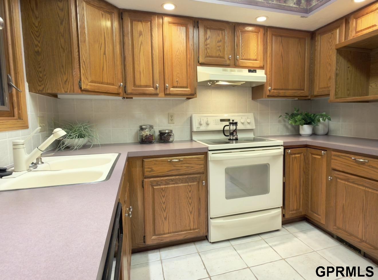 Kitchen with wood cabinets, pale counters, a double sink, and a white electric range.