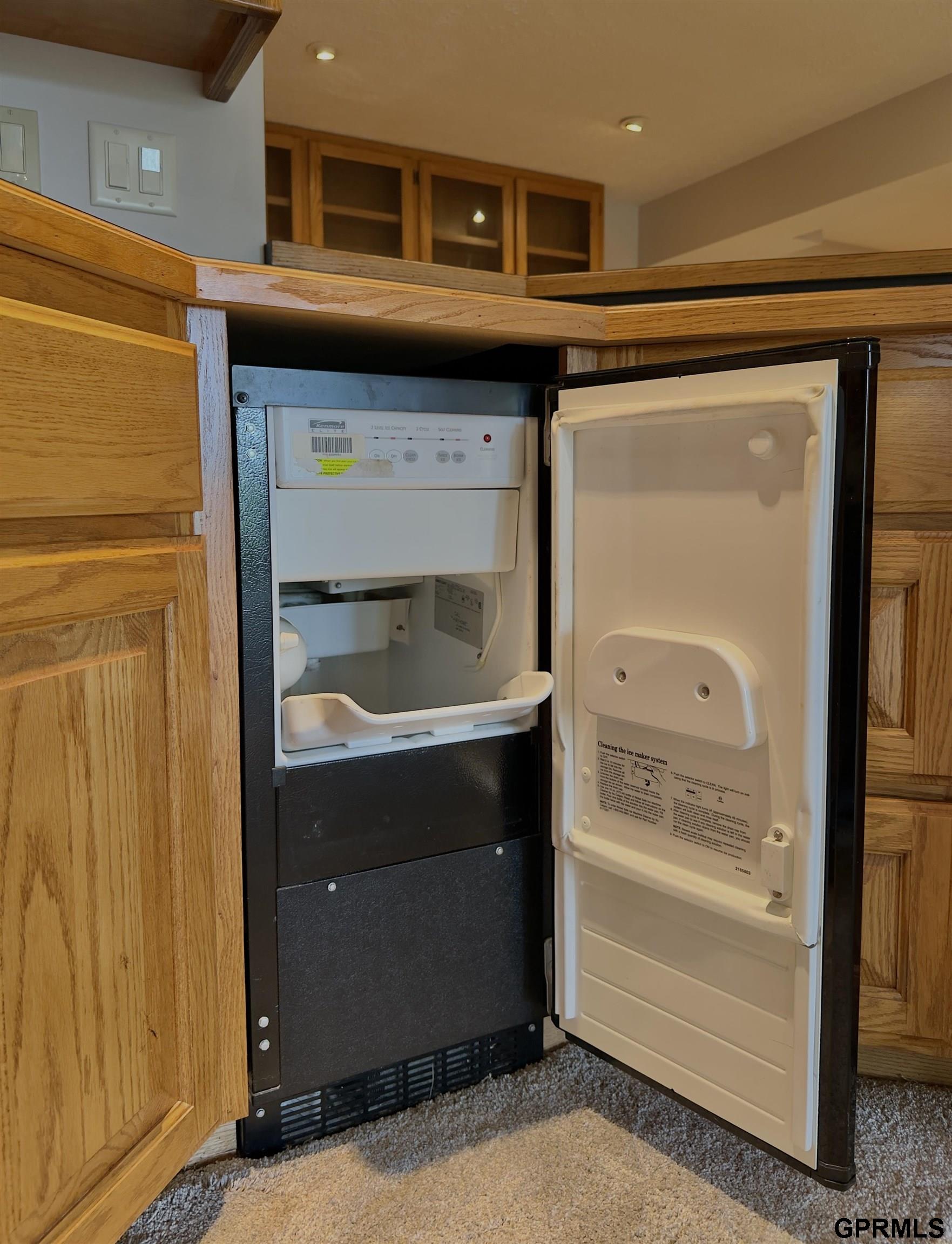 Built-in ice maker open between honey-colored wood cabinets, showing its interior bin and door.