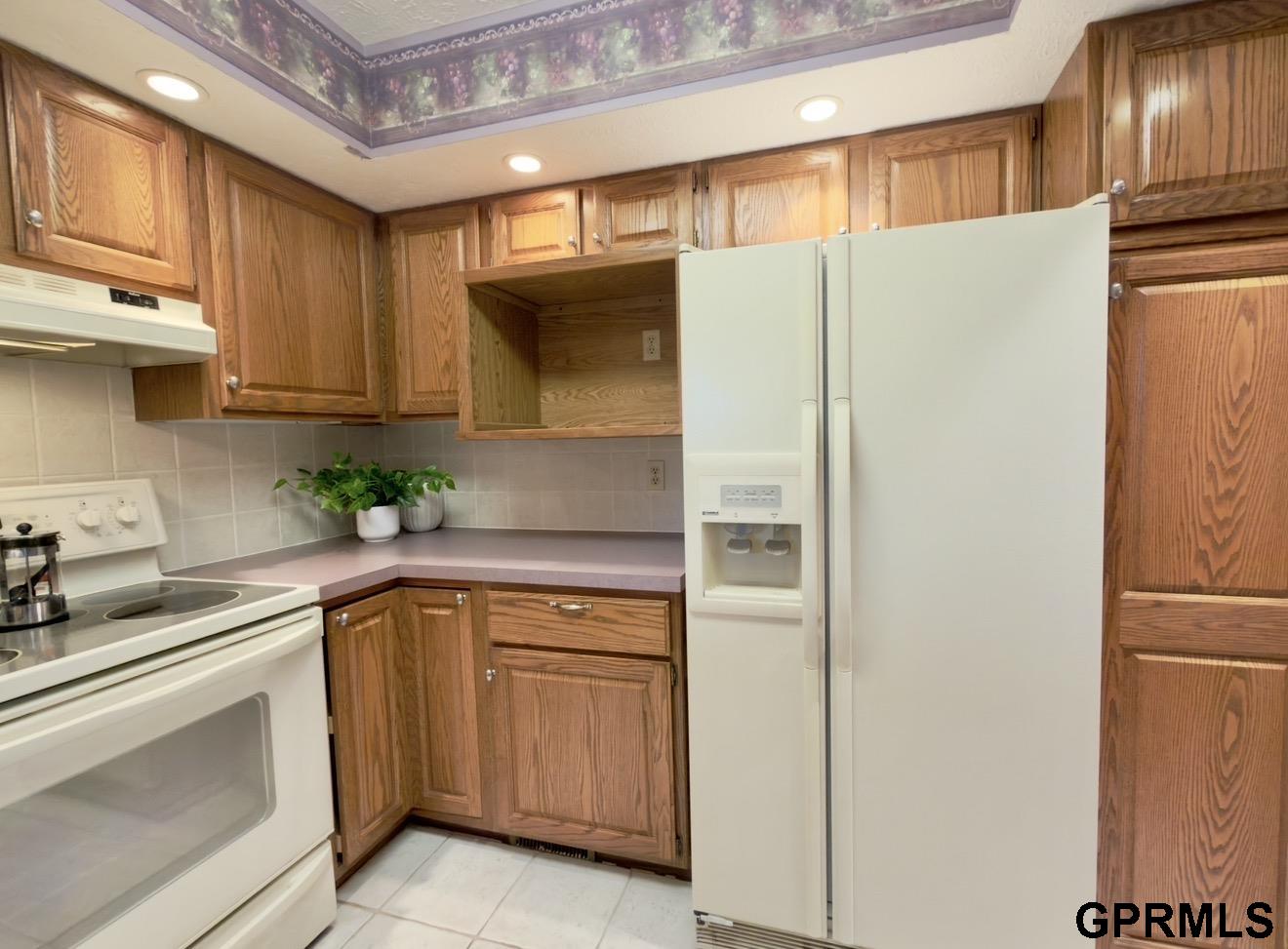 Kitchen with oak cabinets, white appliances, tiled backsplash, and a floral ceiling border.