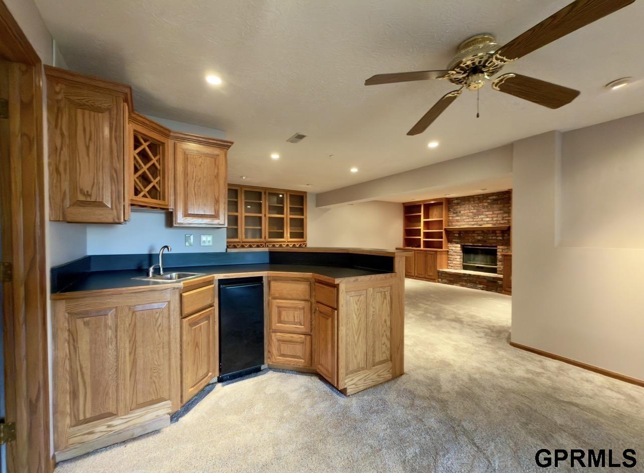 Kitchen with warm wood cabinetry and dark counters opening to a carpeted room with a brick fireplace.