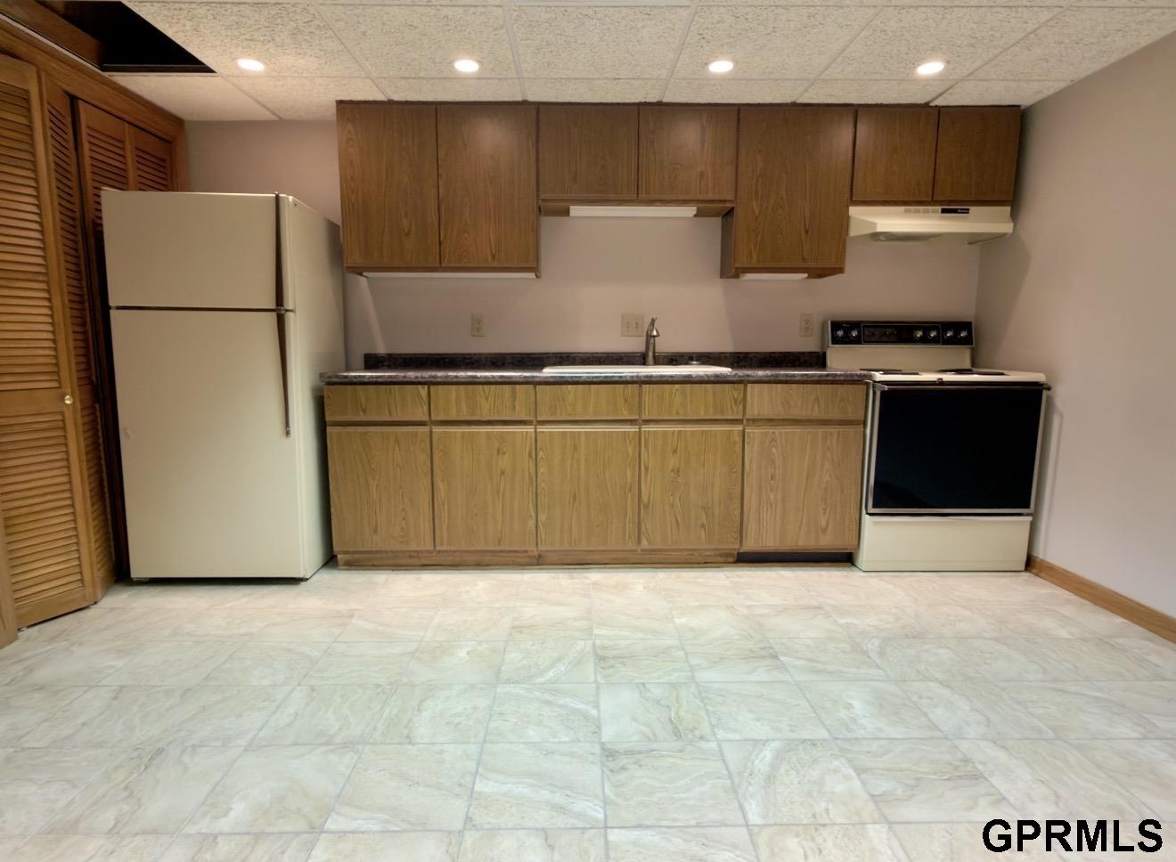 Kitchen with wood cabinets, white refrigerator, electric range, and pale tile flooring.