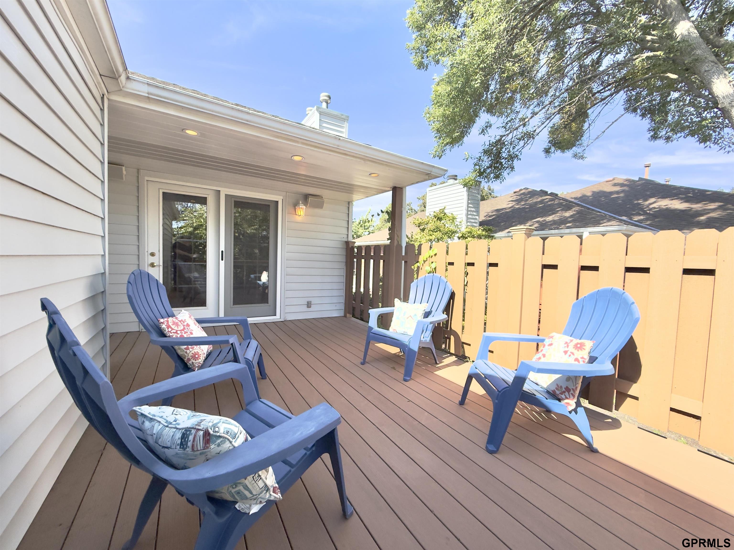 Covered deck with blue Adirondack chairs, brown decking, and a wooden privacy fence.