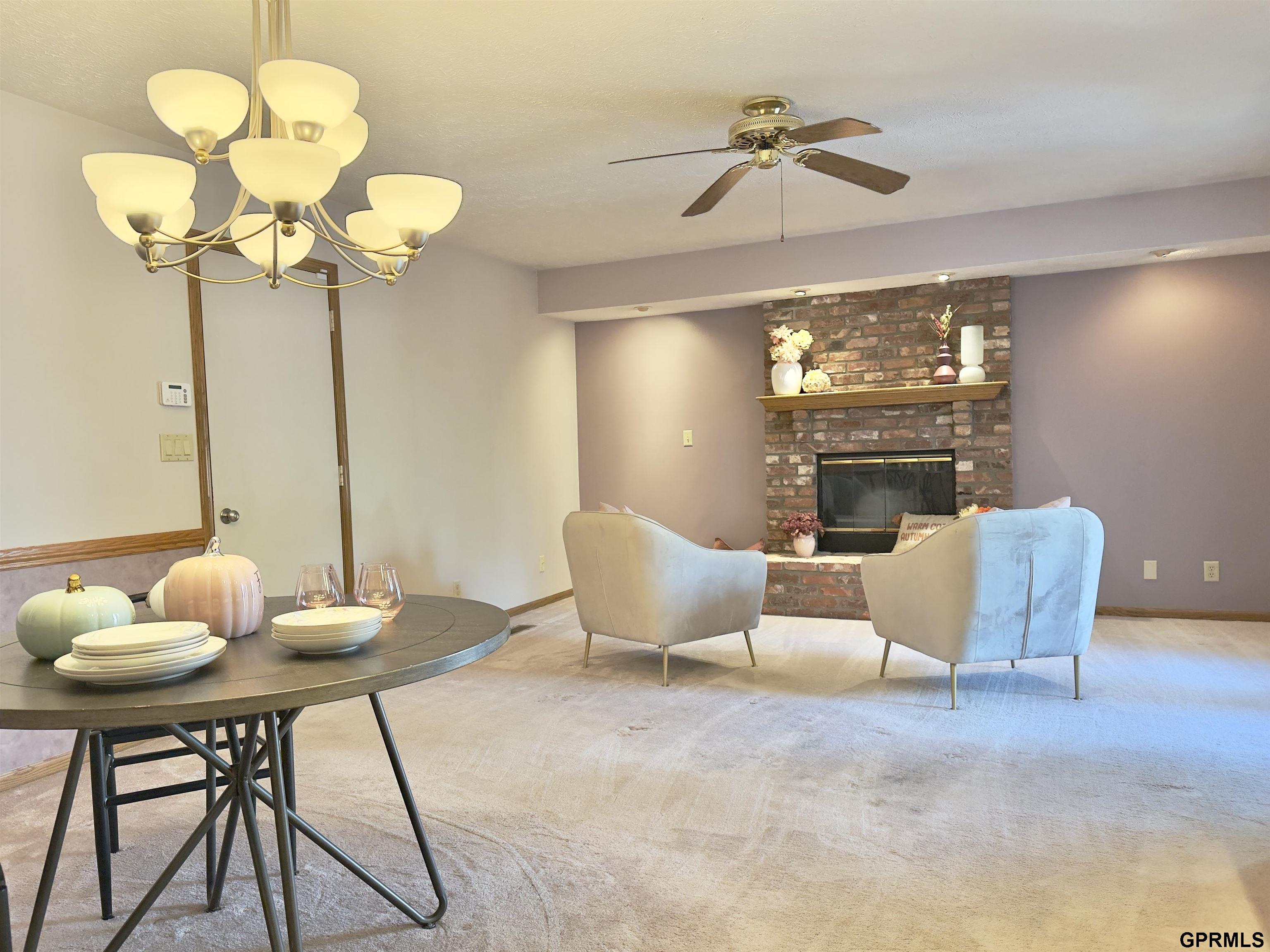 Furnished living room with brick fireplace, two armchairs, and a dining table in the foreground.