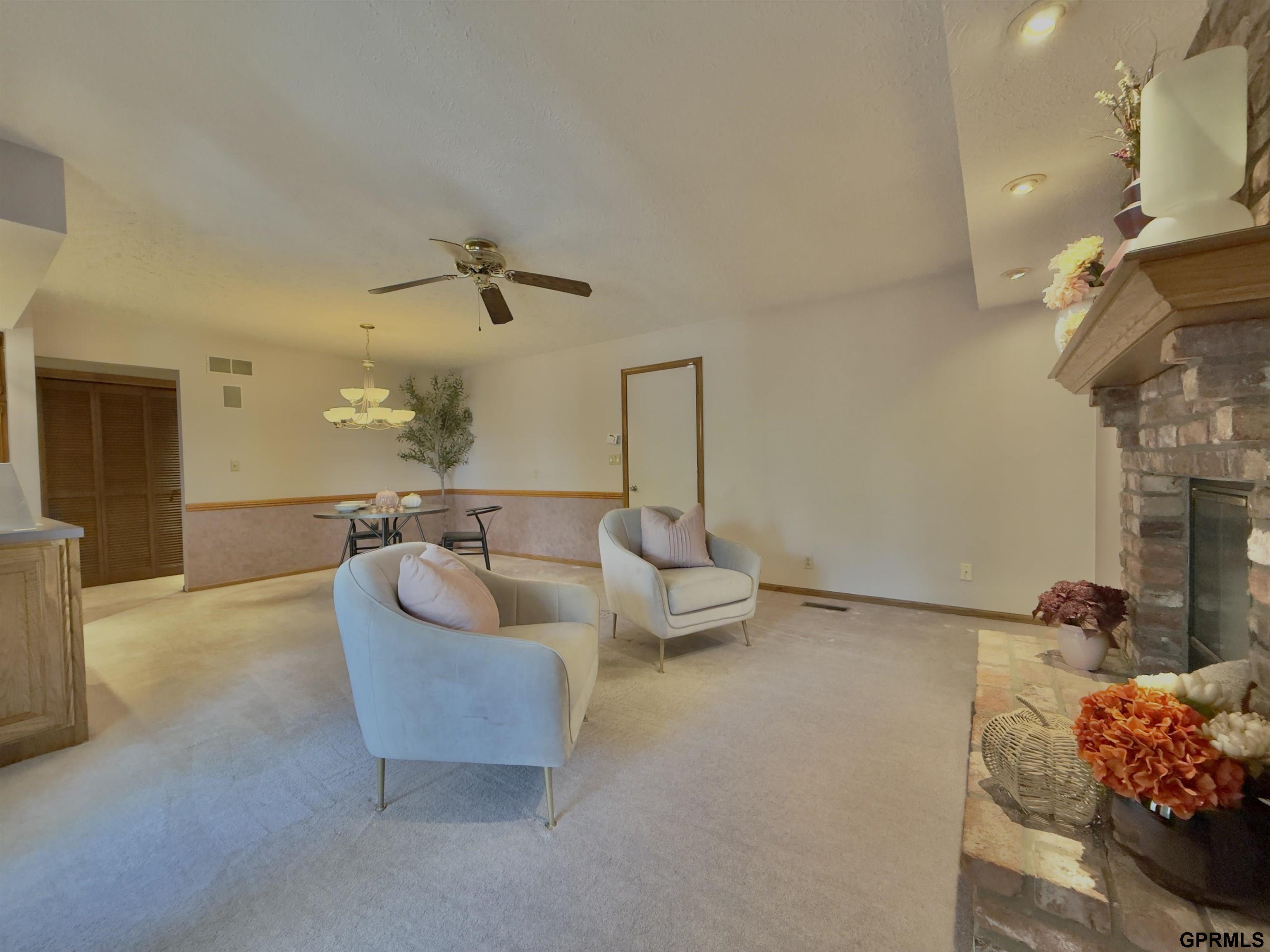 Living room with pale armchairs, a dining nook, and a stone fireplace with a wooden mantel.