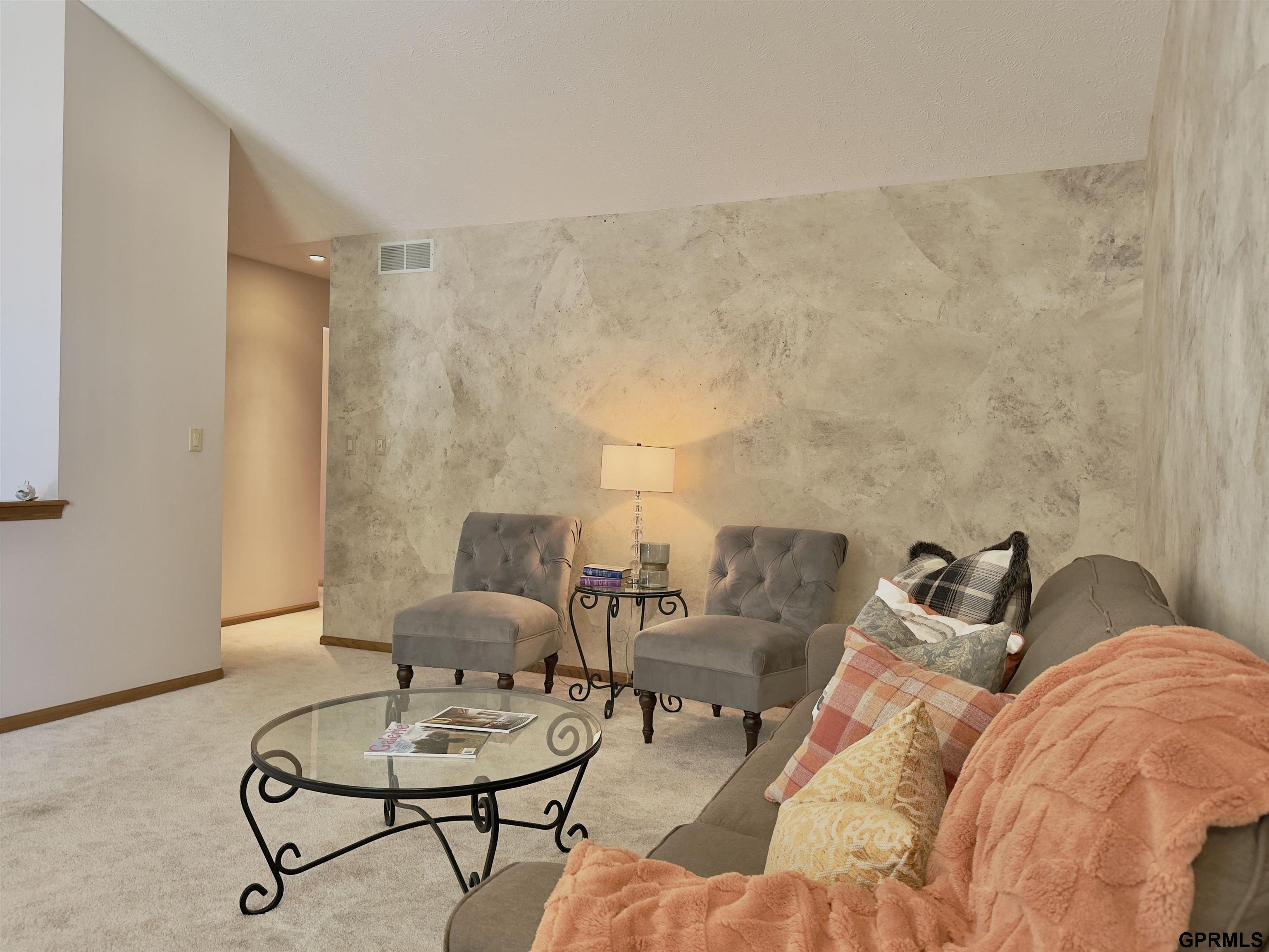 Furnished living room with a stone feature wall, gray armchairs, and a sofa with colorful pillows.
