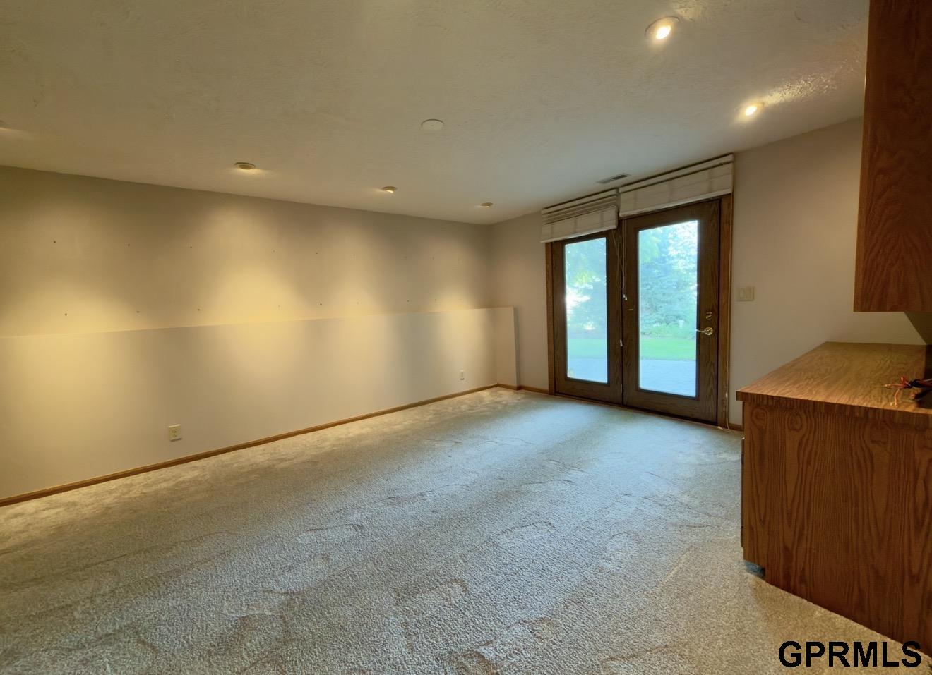 Empty carpeted room with wood-trimmed glass doors opening to the yard.