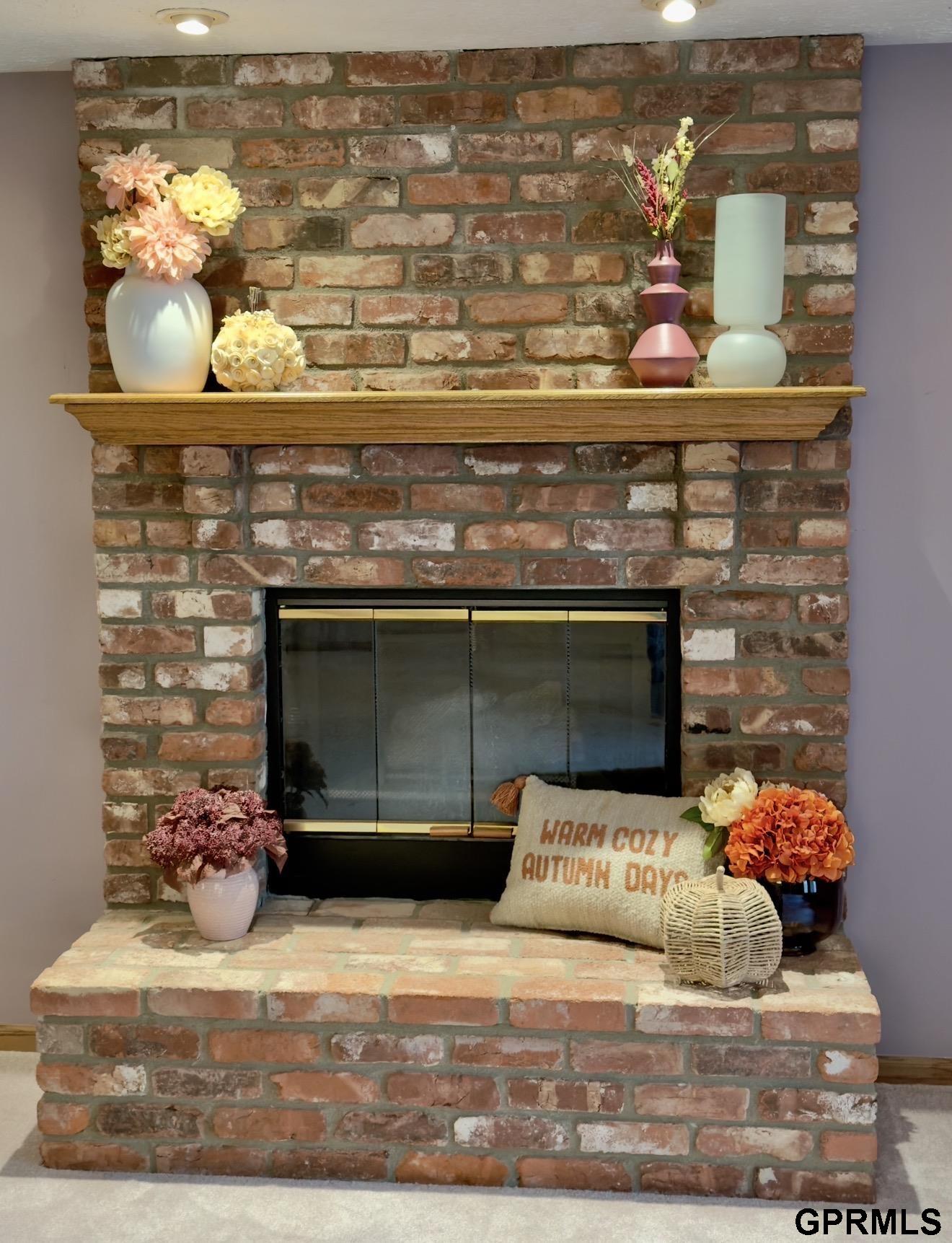 Brick fireplace with black glass screen, wooden mantel, and autumn flowers and decor.