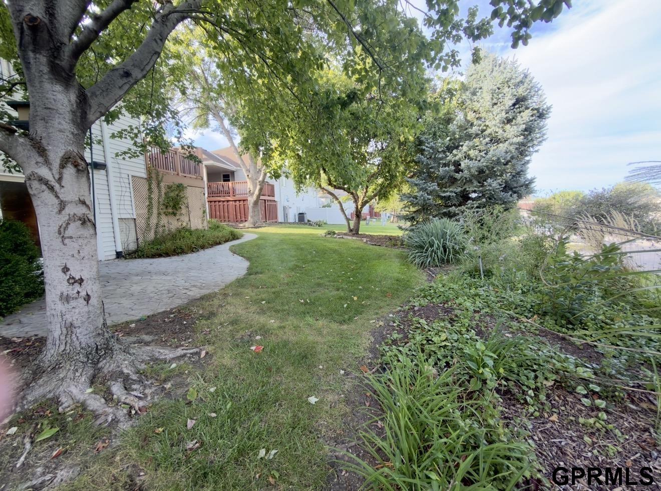 Backyard with a curved stone walkway, mature trees, lawn, and raised wooden deck.