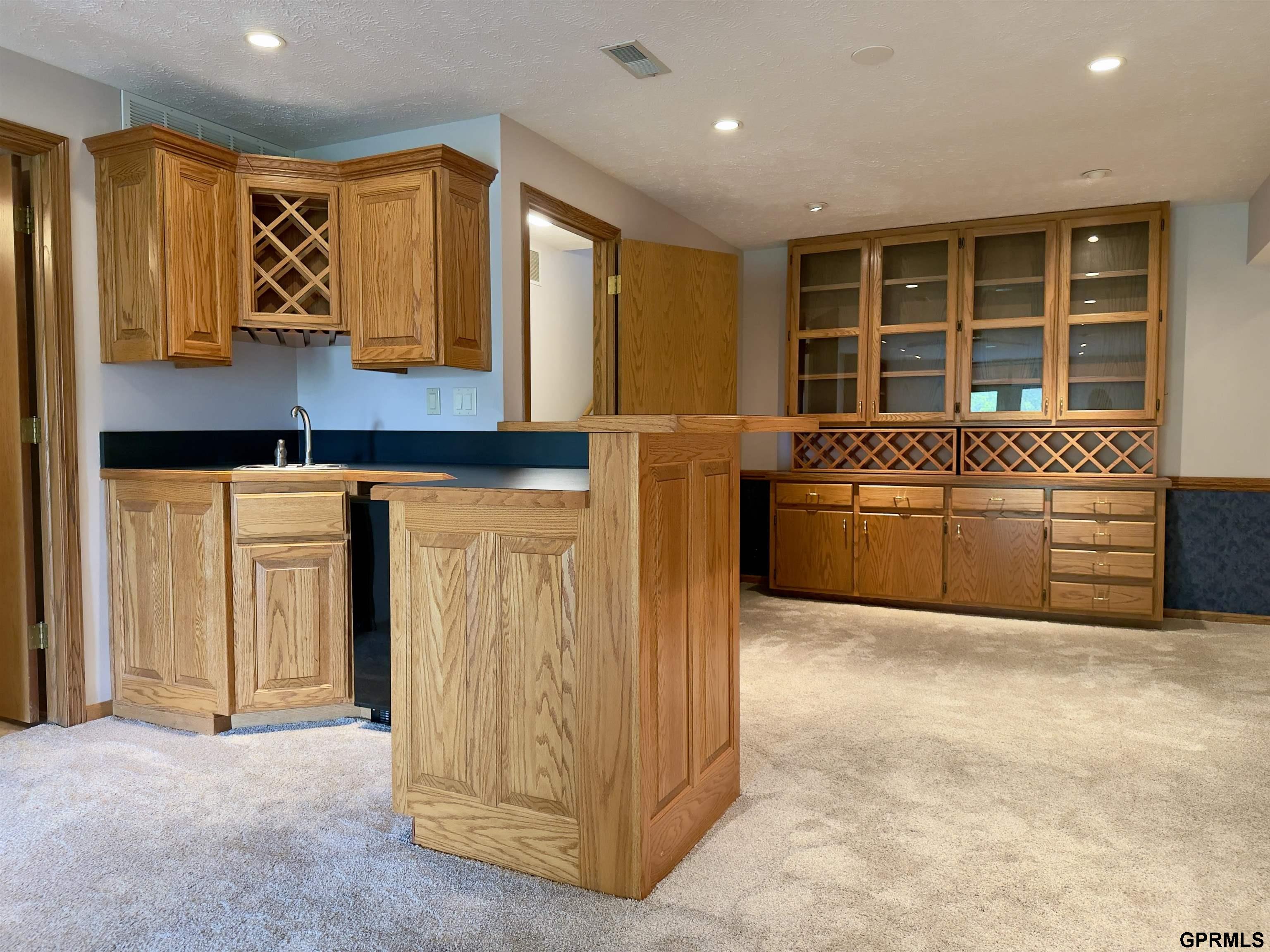 Oak wet bar with sink, raised counter, glass-front cabinets, and built-in wine racks.
