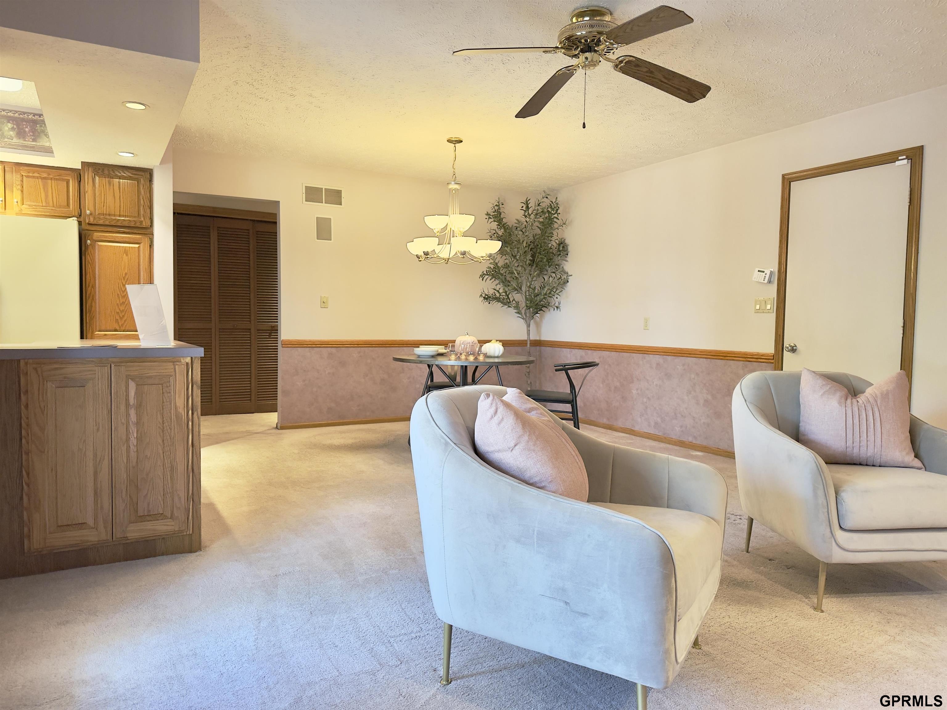 Living and dining area with pale chairs, wood cabinetry, a round table, and ceiling fan.