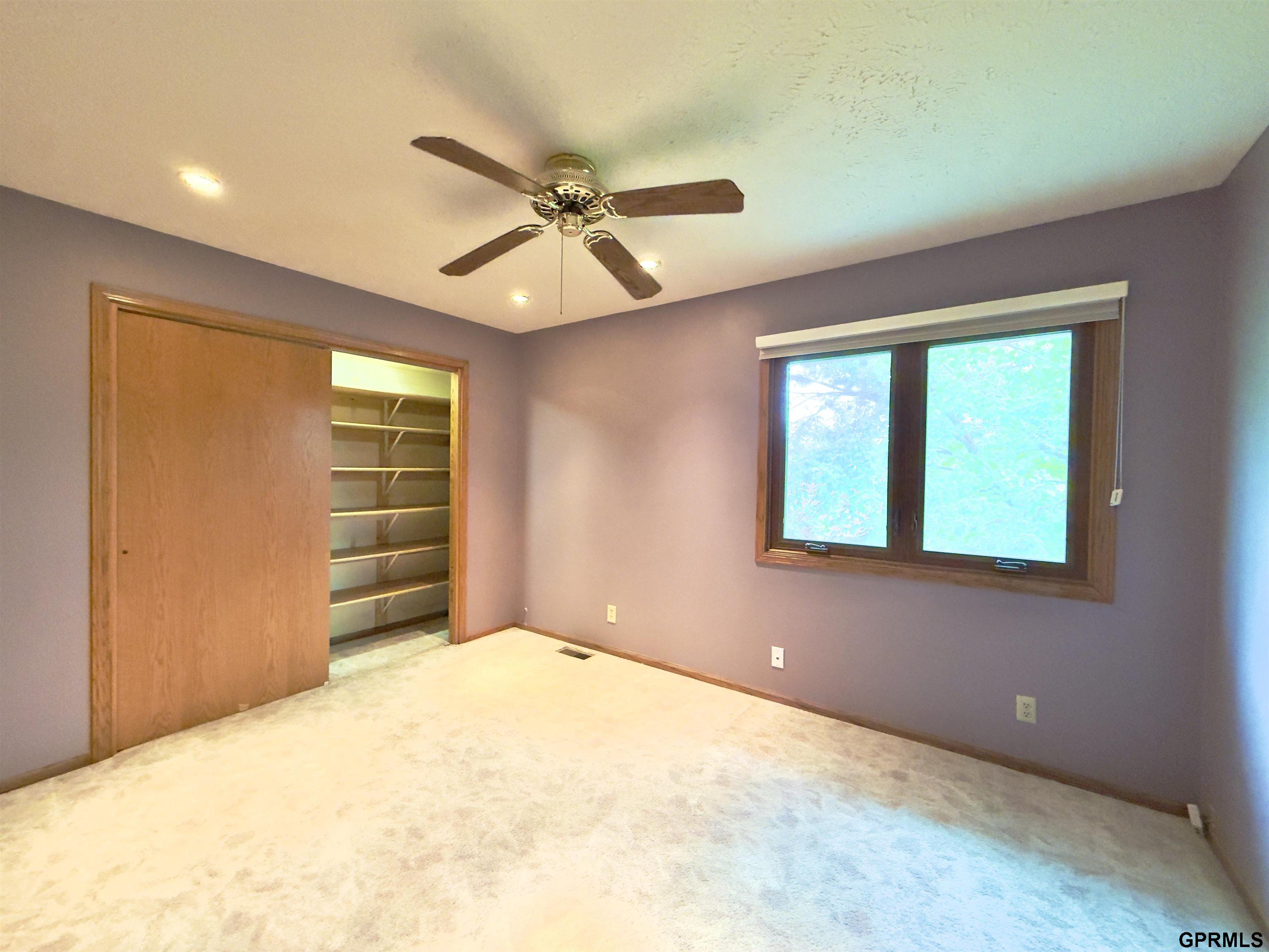 Vacant bedroom with a ceiling fan, large window, and partly open closet with shelves.