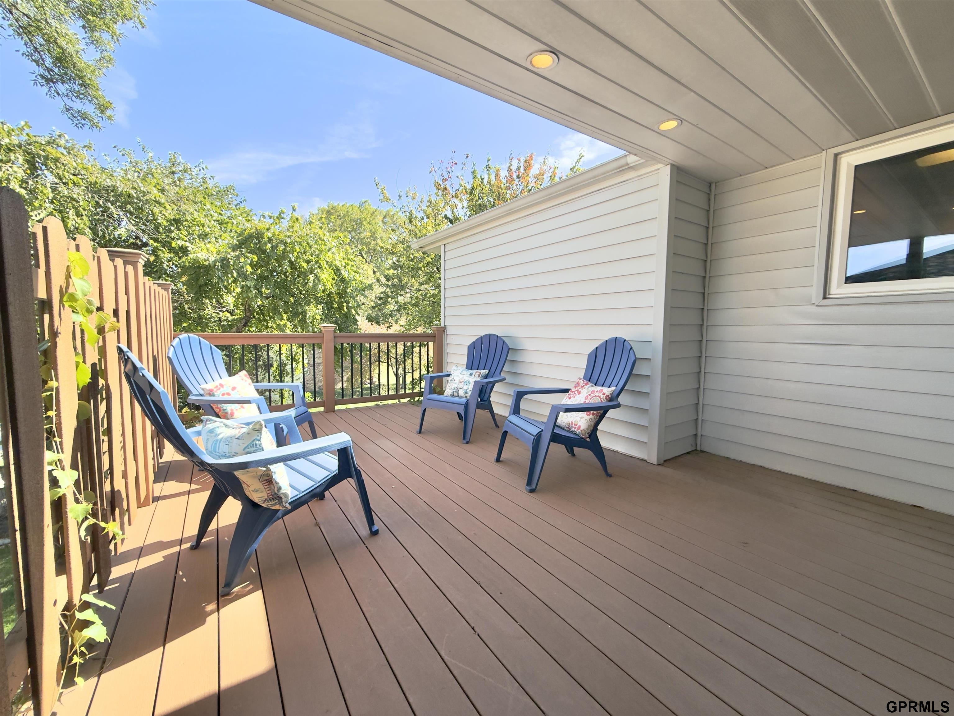 Covered deck with four blue chairs, brown flooring, and leafy trees beyond the railing.