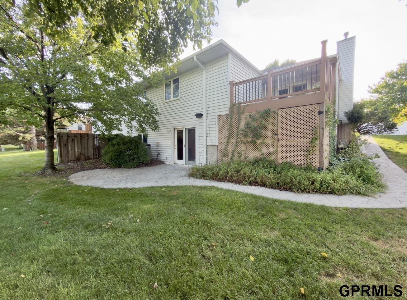 Rear of a two-story home with a raised deck, lattice skirting, and curved paver patio.