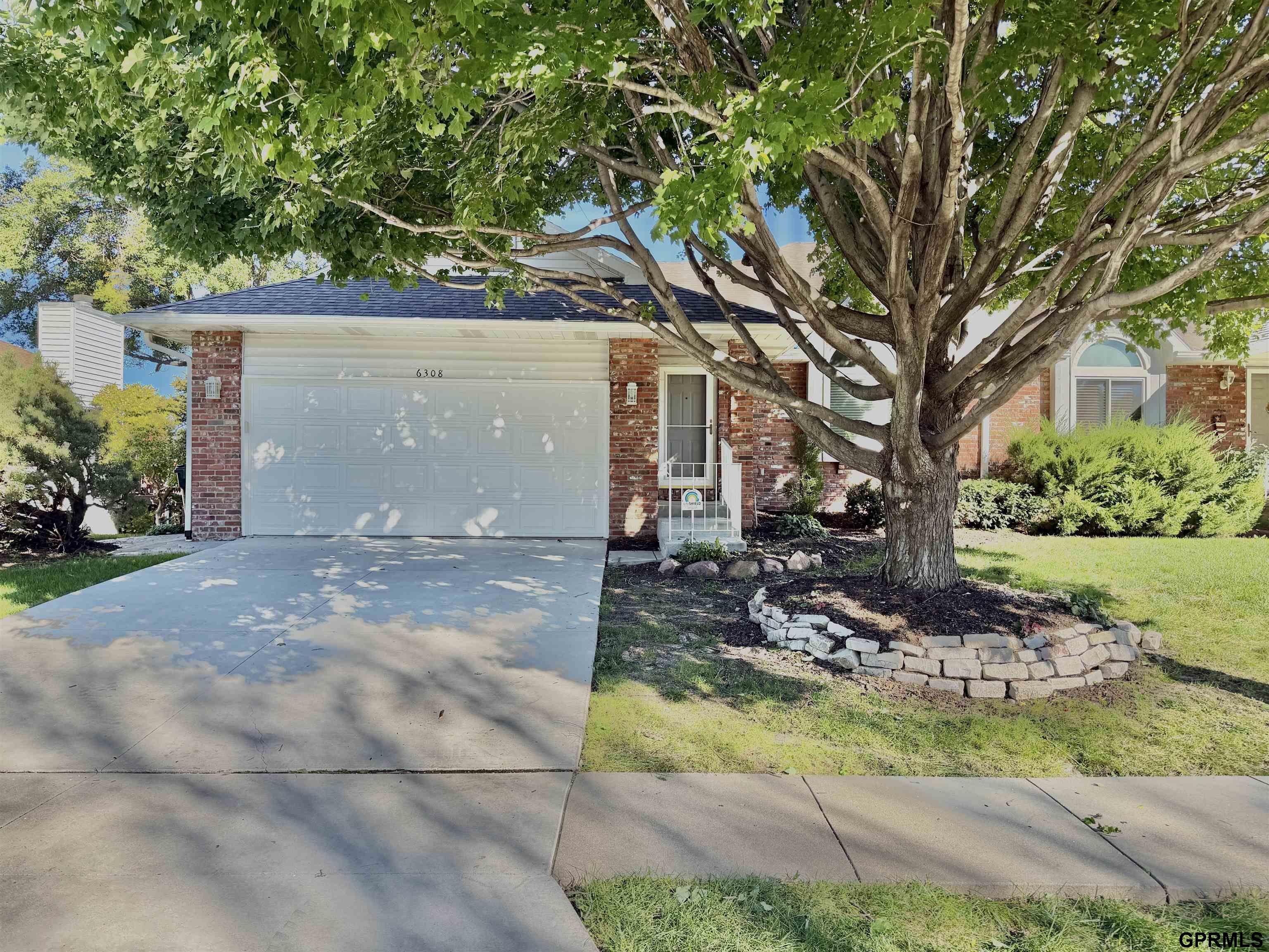 Brick house with a two-car garage and a large shade tree in the front yard.