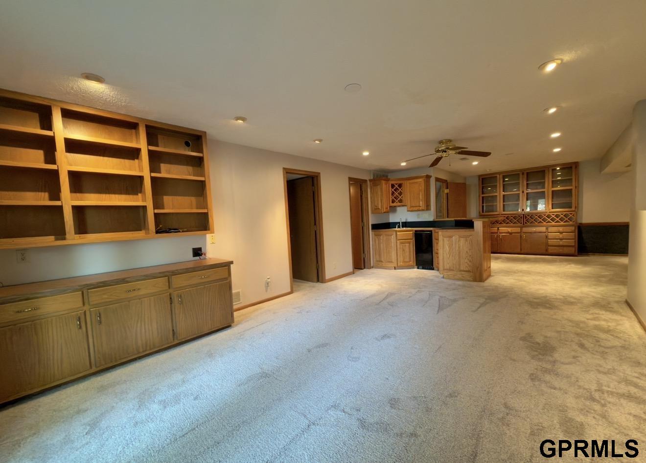 Carpeted basement recreation room with built-in cabinetry and a kitchenette with wine racks.