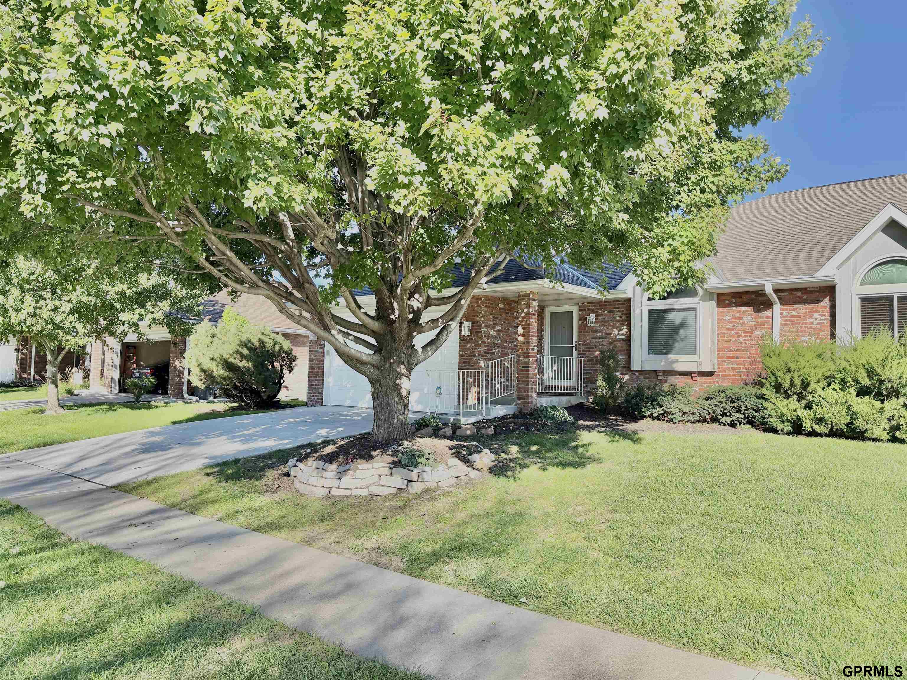 Red-brick house with white trim and a large leafy tree shading the front yard.