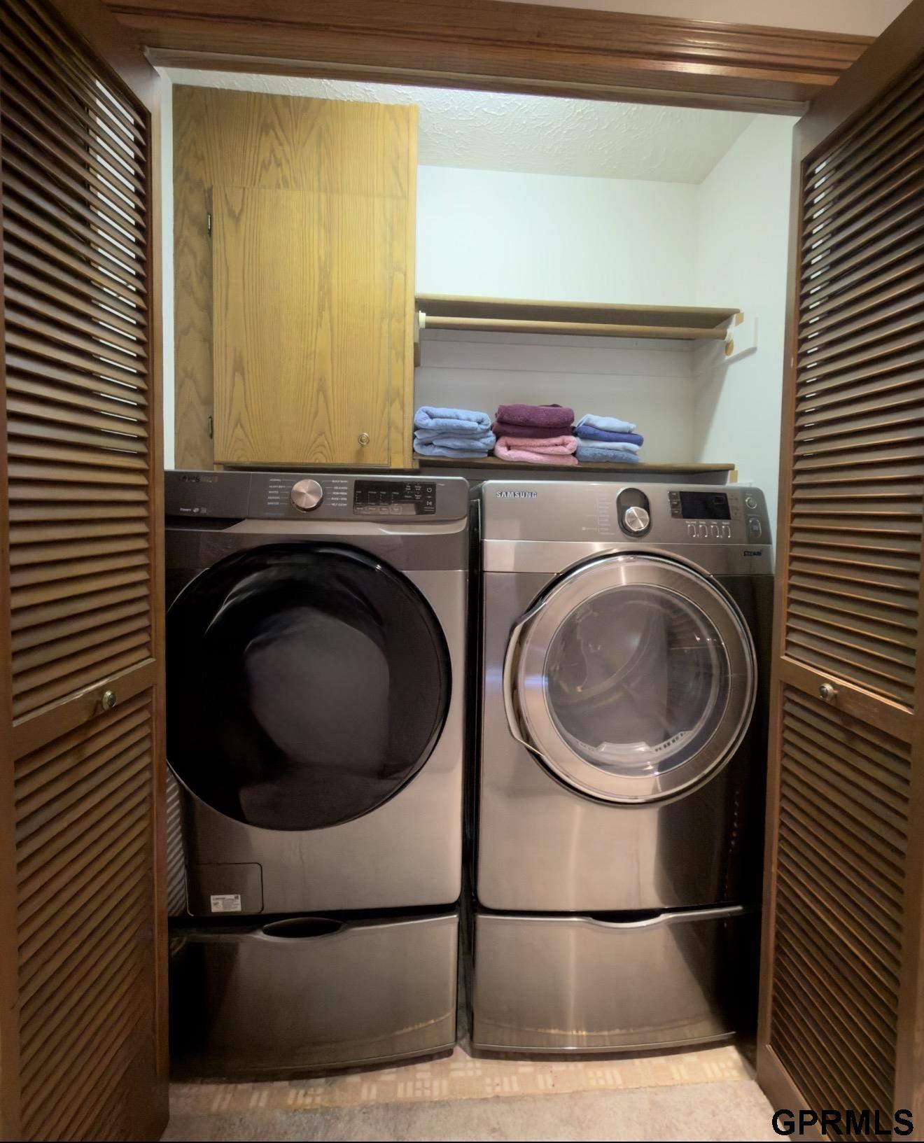 Laundry closet with front-loading washer and dryer, wooden cabinetry, and folded towels.