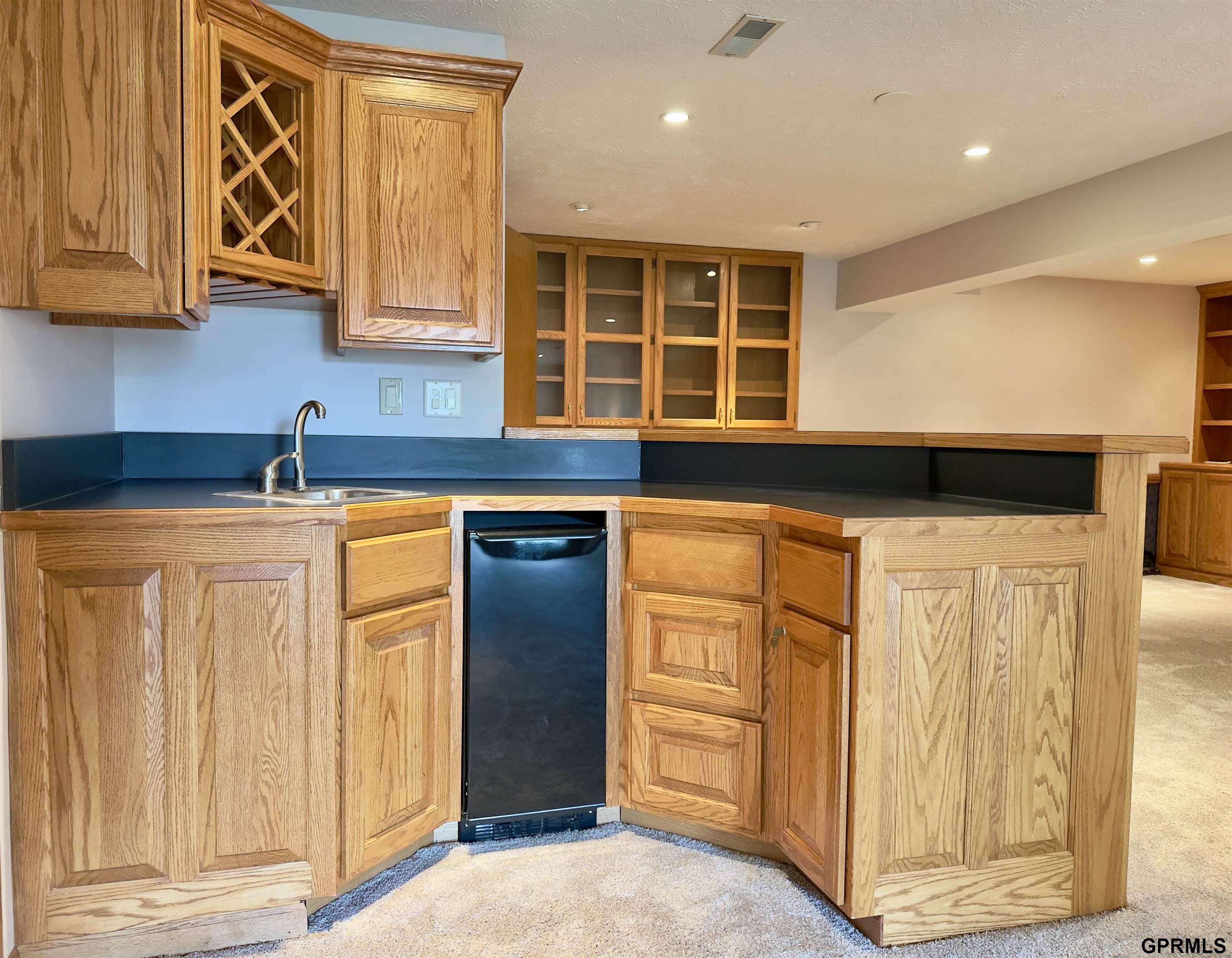 Kitchen with honey-toned wood cabinets, dark counters, and a built-in under-counter refrigerator.