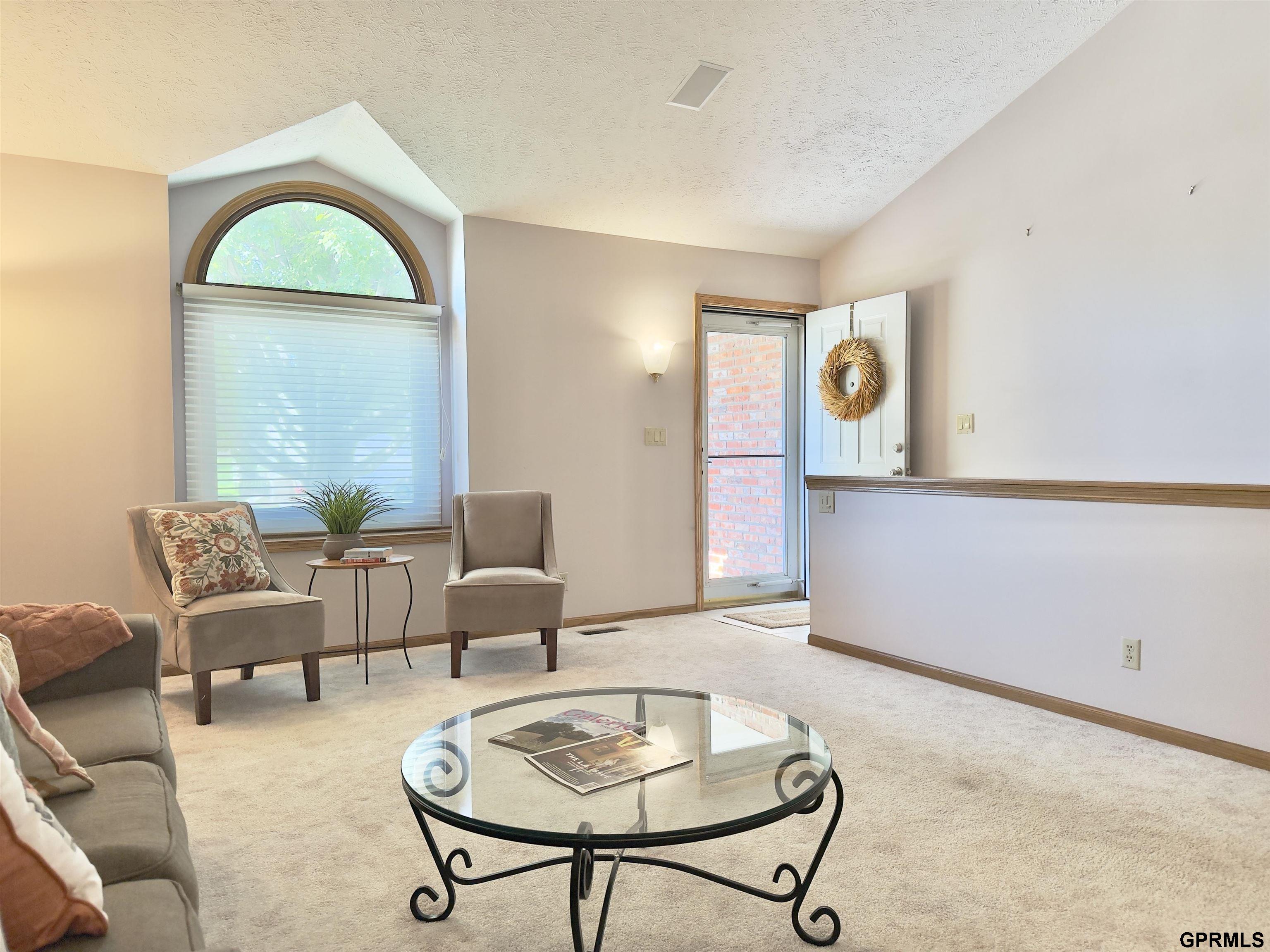 Living room with a large arched window, two accent chairs, and a glass coffee table.