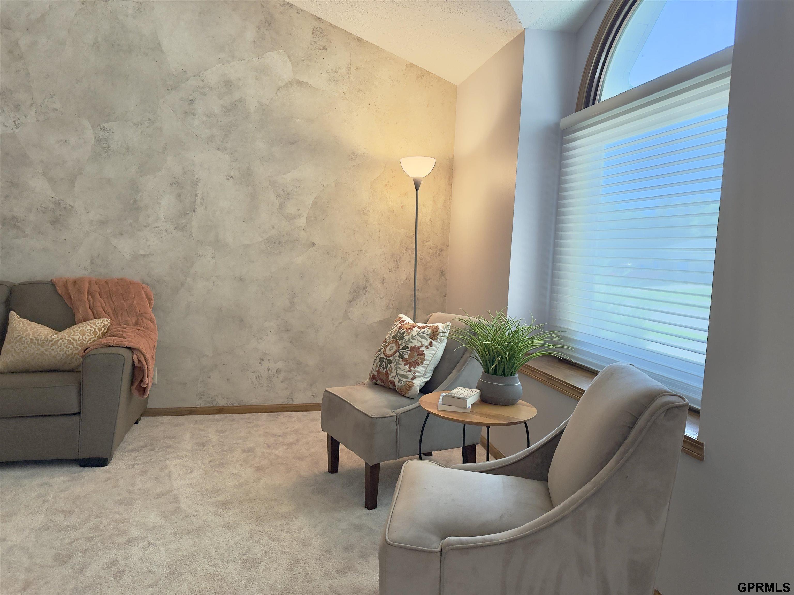 Furnished sitting room with gray seating, a textured accent wall, and a large arched window.