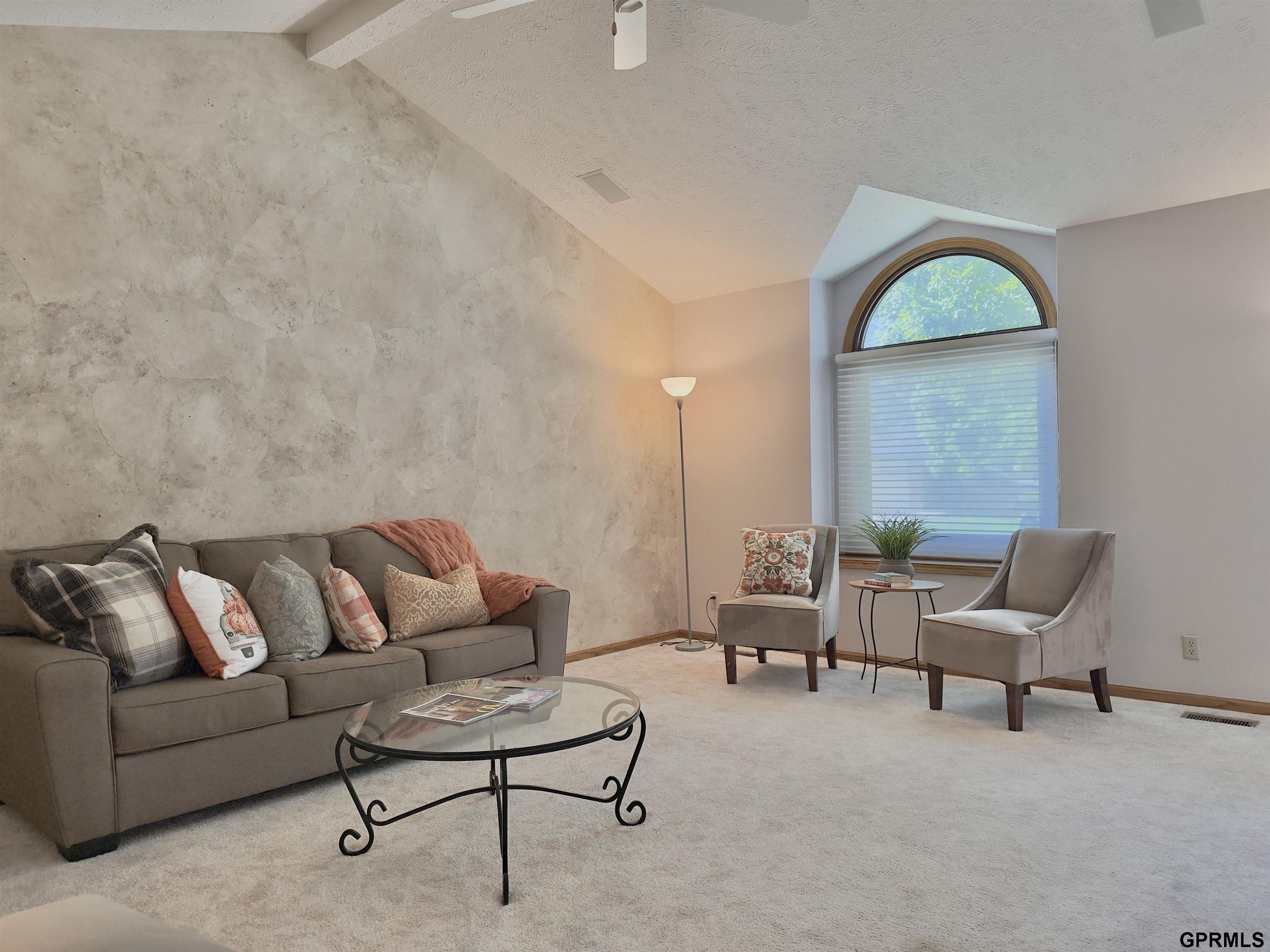 Furnished living room with a textured stone accent wall and tall arched window.