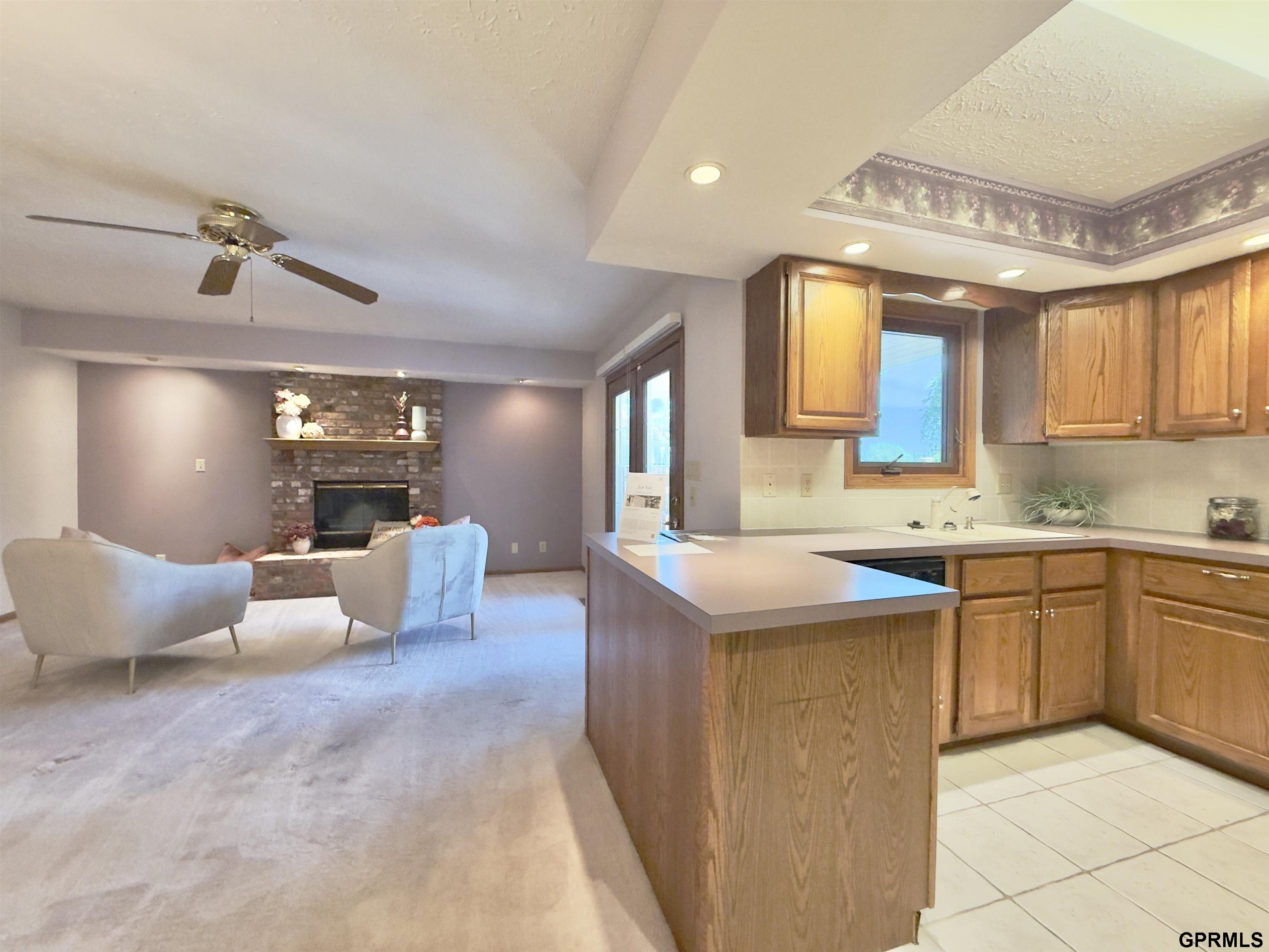 Open kitchen with a wood peninsula island overlooking a carpeted living area and stone fireplace.