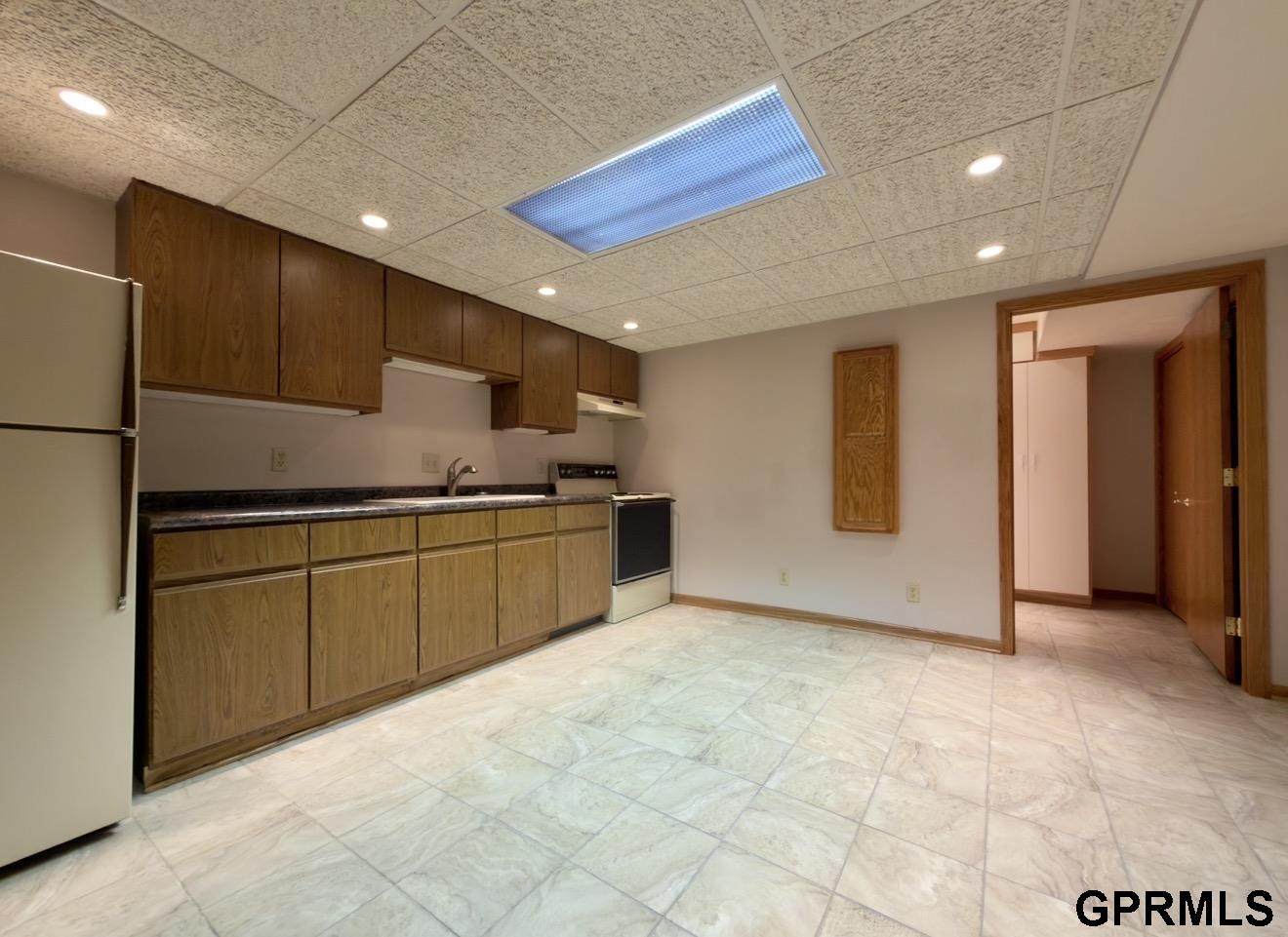 Kitchen with wood cabinets, refrigerator, stove, and light tile flooring.