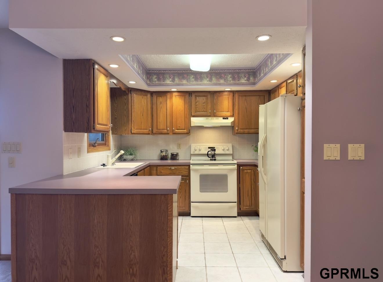 Kitchen with wood cabinetry, white appliances, and a tiled floor.