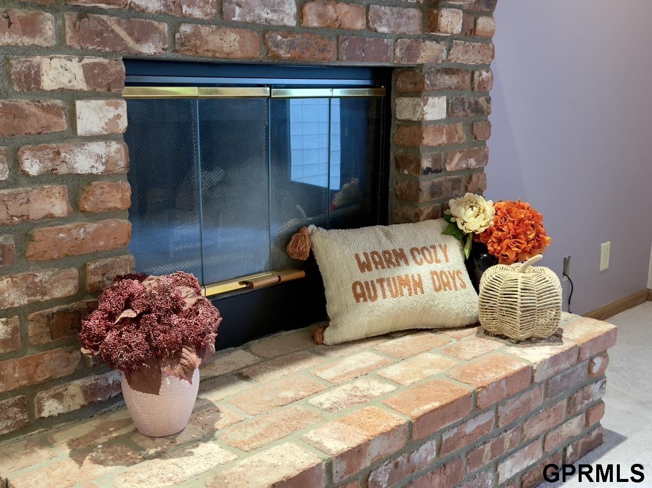 Brick fireplace with glass screen, autumn pillow, flowers, and woven pumpkin on the hearth.