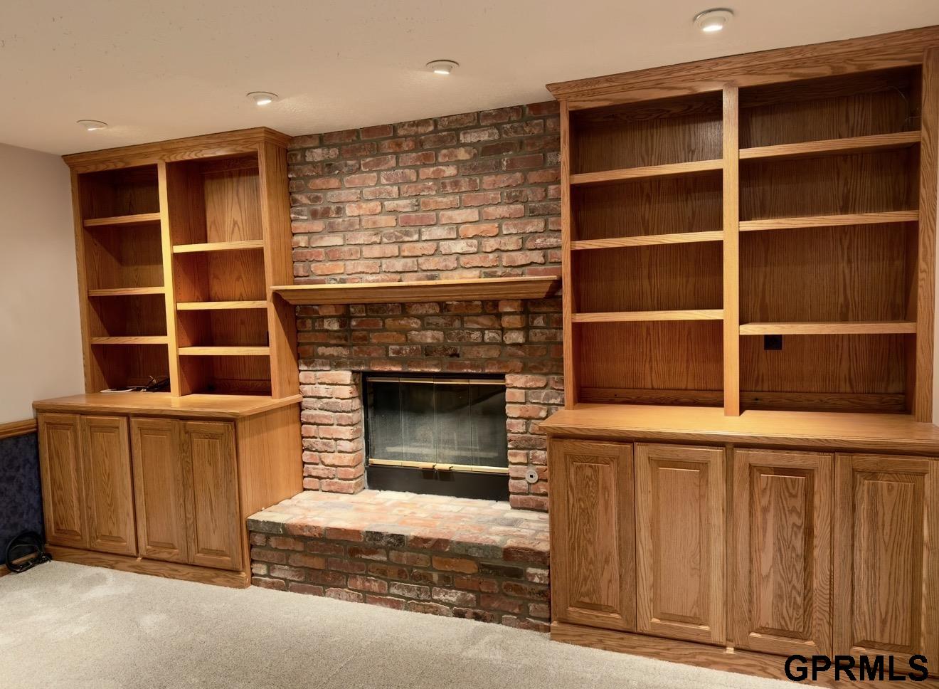 Brick fireplace with raised hearth, flanked by built-in oak cabinets and bookshelves.