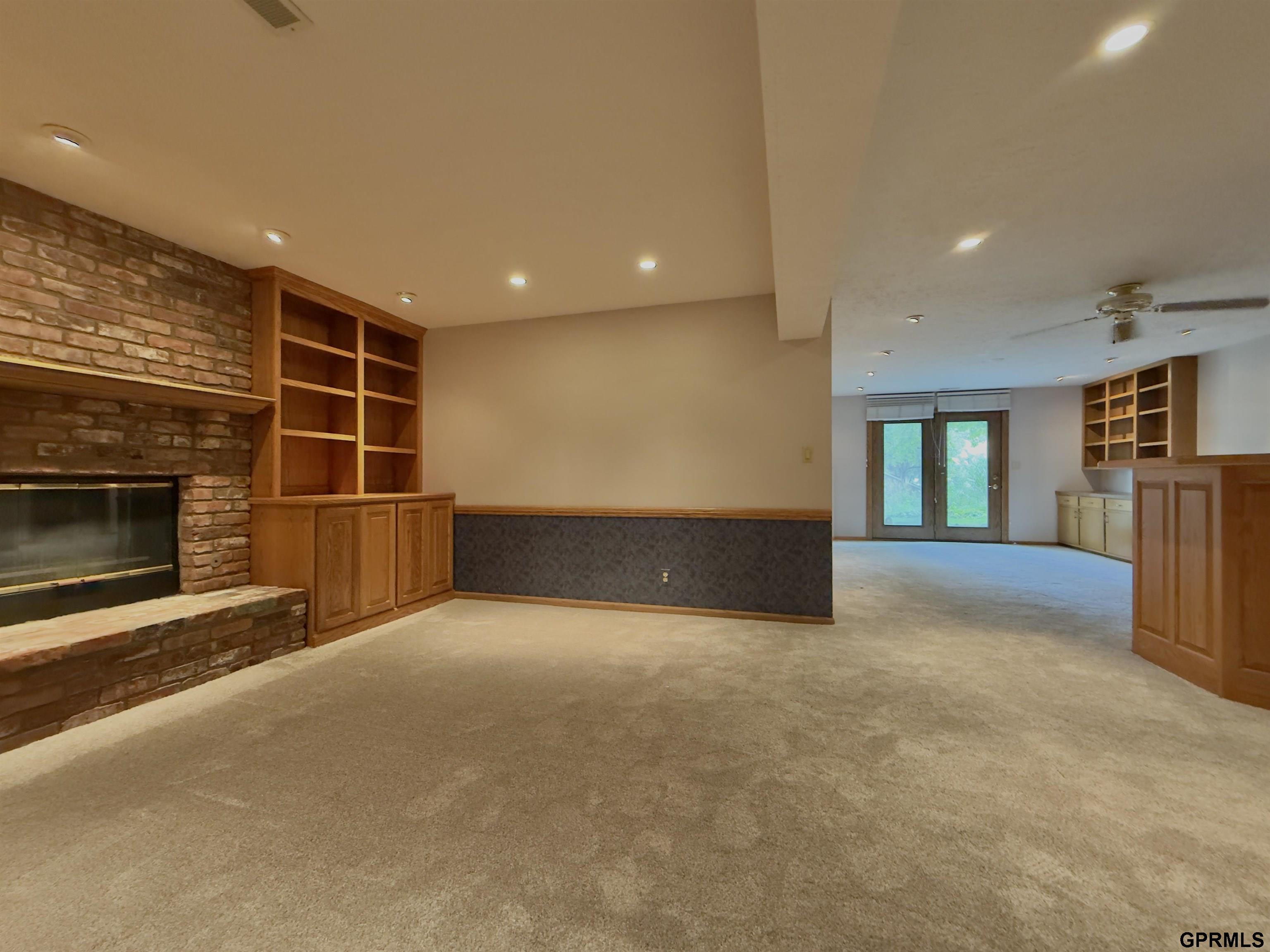 Unfurnished living area with a brick fireplace, built-in wood shelving, and glass doors to the adjoining room.