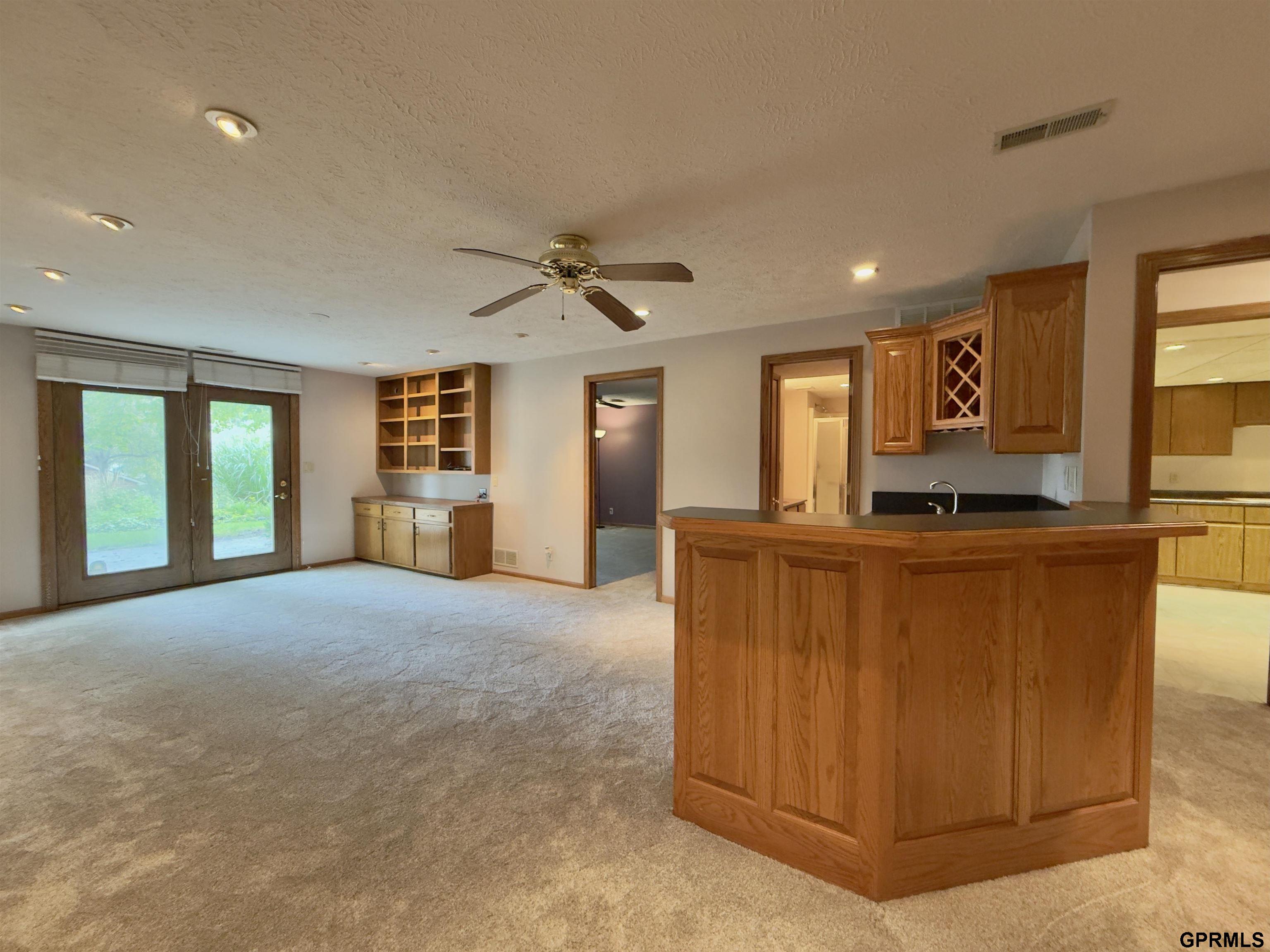 Open living area with beige carpet, sliding glass doors, built-in shelves, and a large wood kitchen peninsula.