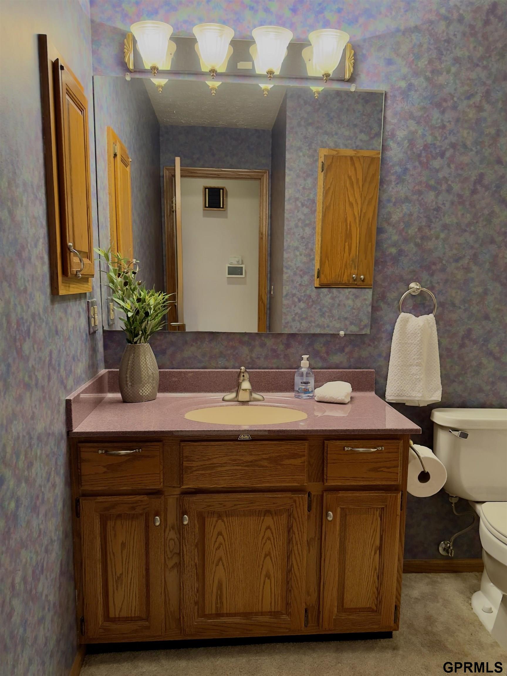 Bathroom vanity with an oak cabinet, pink countertop, large mirror, and purple patterned wallpaper.