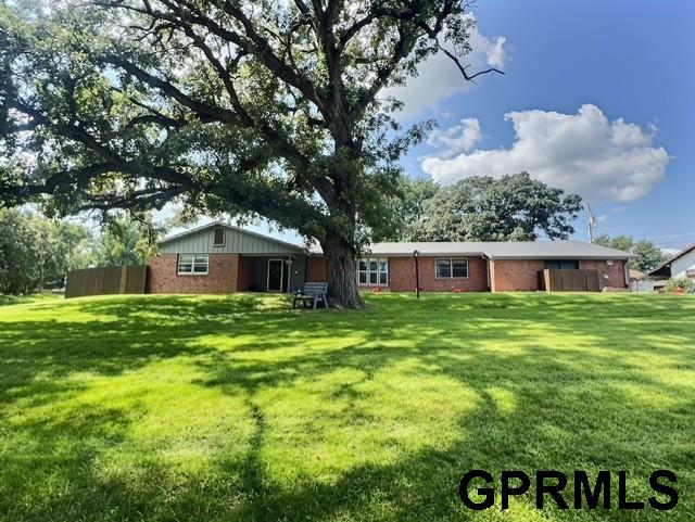 Brick ranch home behind a broad lawn, partly shaded by a large mature tree.