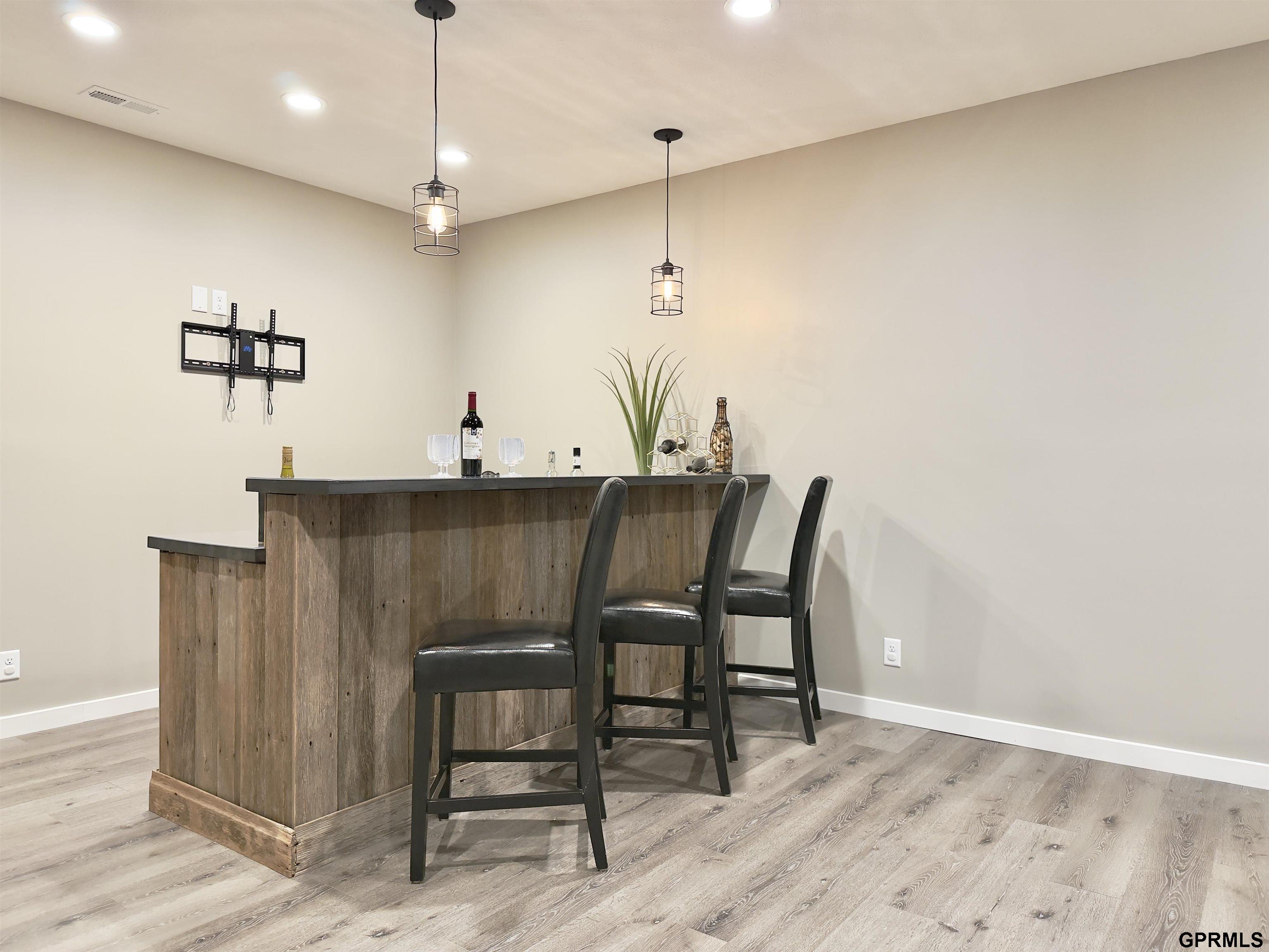 Bar area with a dark wood counter, three black stools, and cage-style pendant lights.
