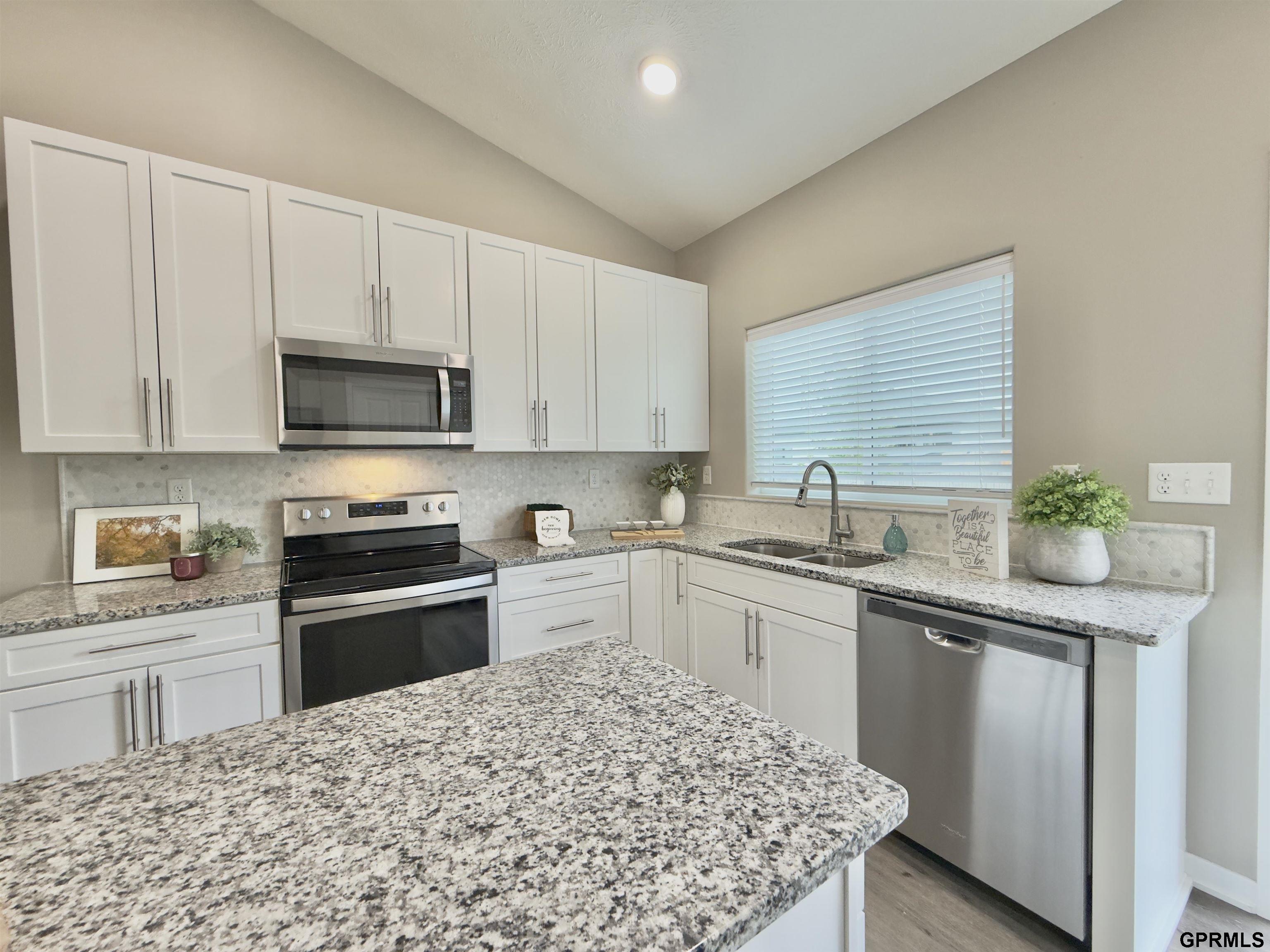 Kitchen with white cabinets, granite island, stainless steel appliances, and a double-basin sink by the window.