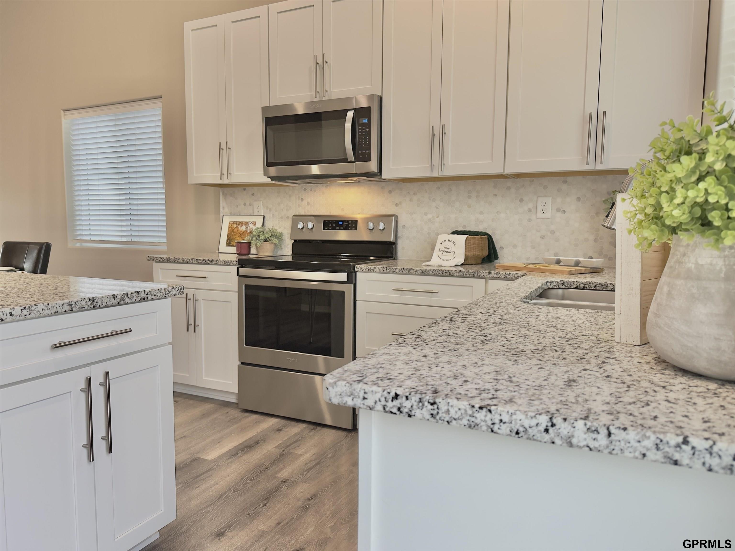 Kitchen with white cabinetry, stainless appliances, granite countertops, and a large island.