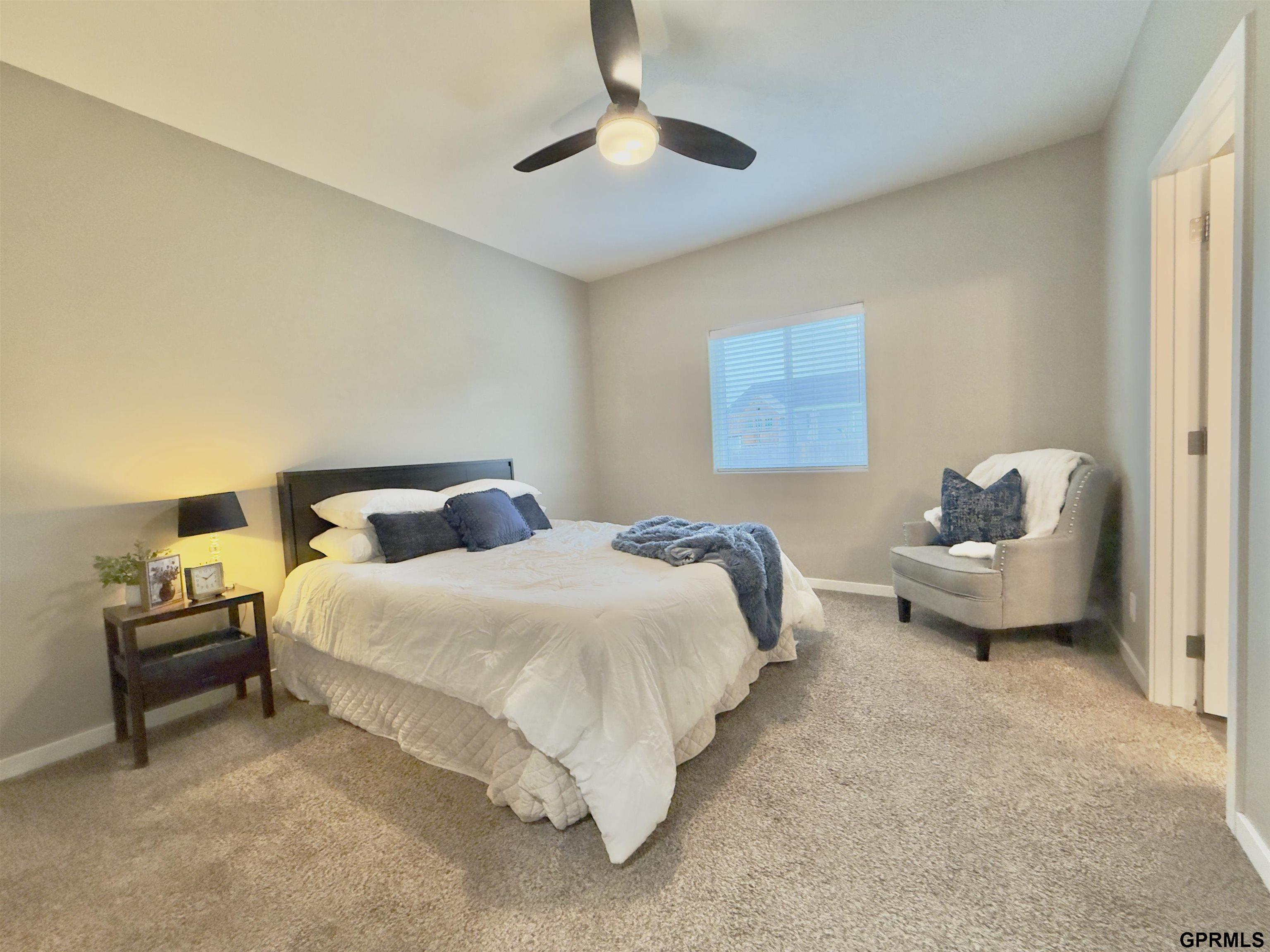 Bedroom with a white bed, blue accents, ceiling fan, and gray armchair by the window.