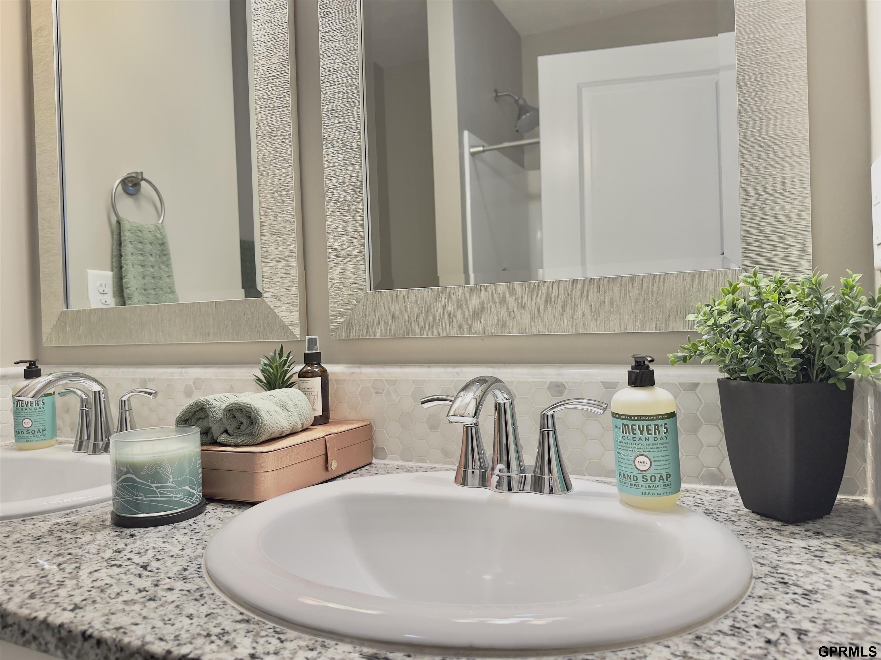 Bathroom vanity with a white oval sink, chrome faucet, granite counter, and hexagonal tile backsplash.