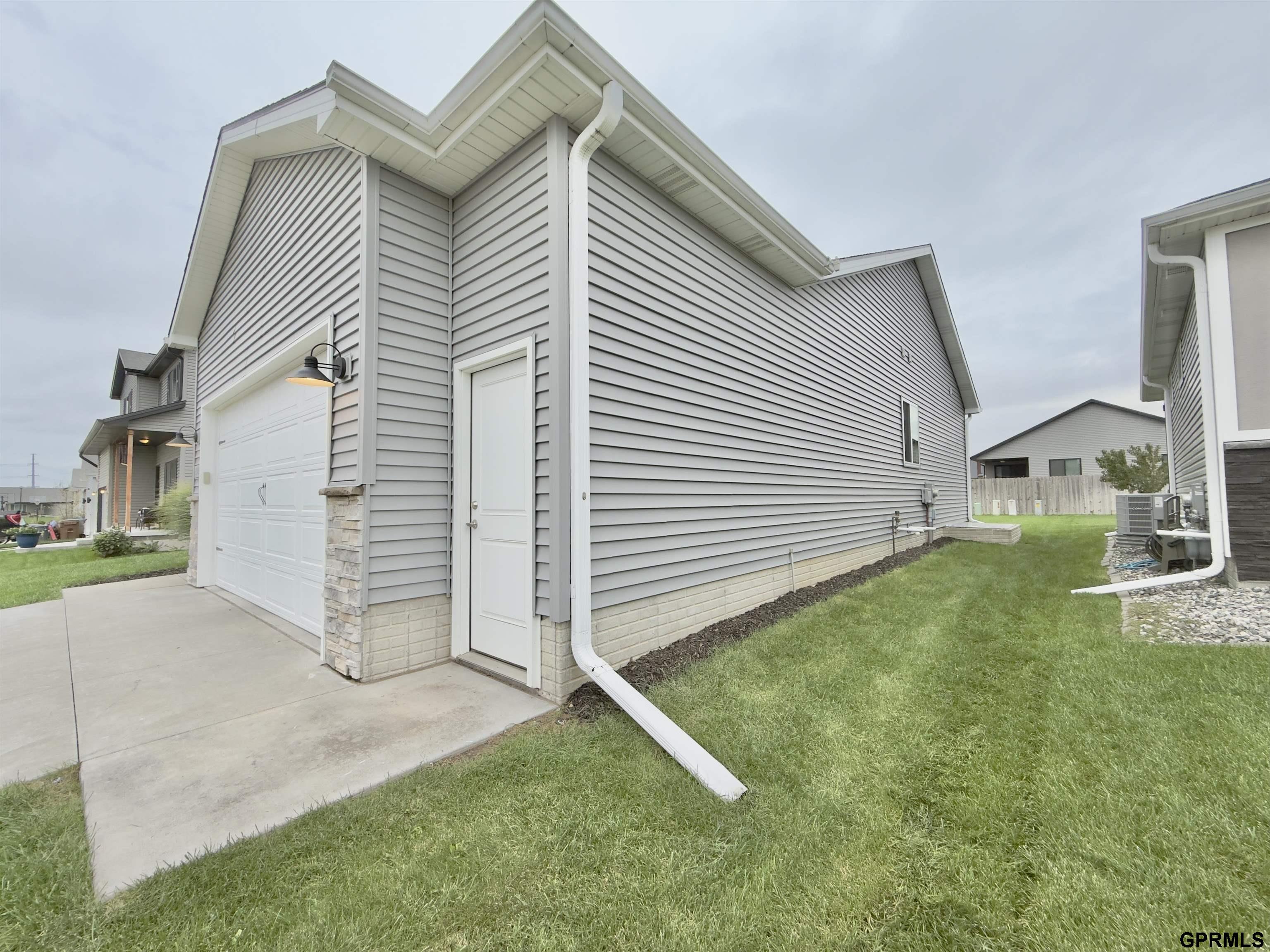 Gray-sided house with a white garage door, side entrance, and broad lawn.
