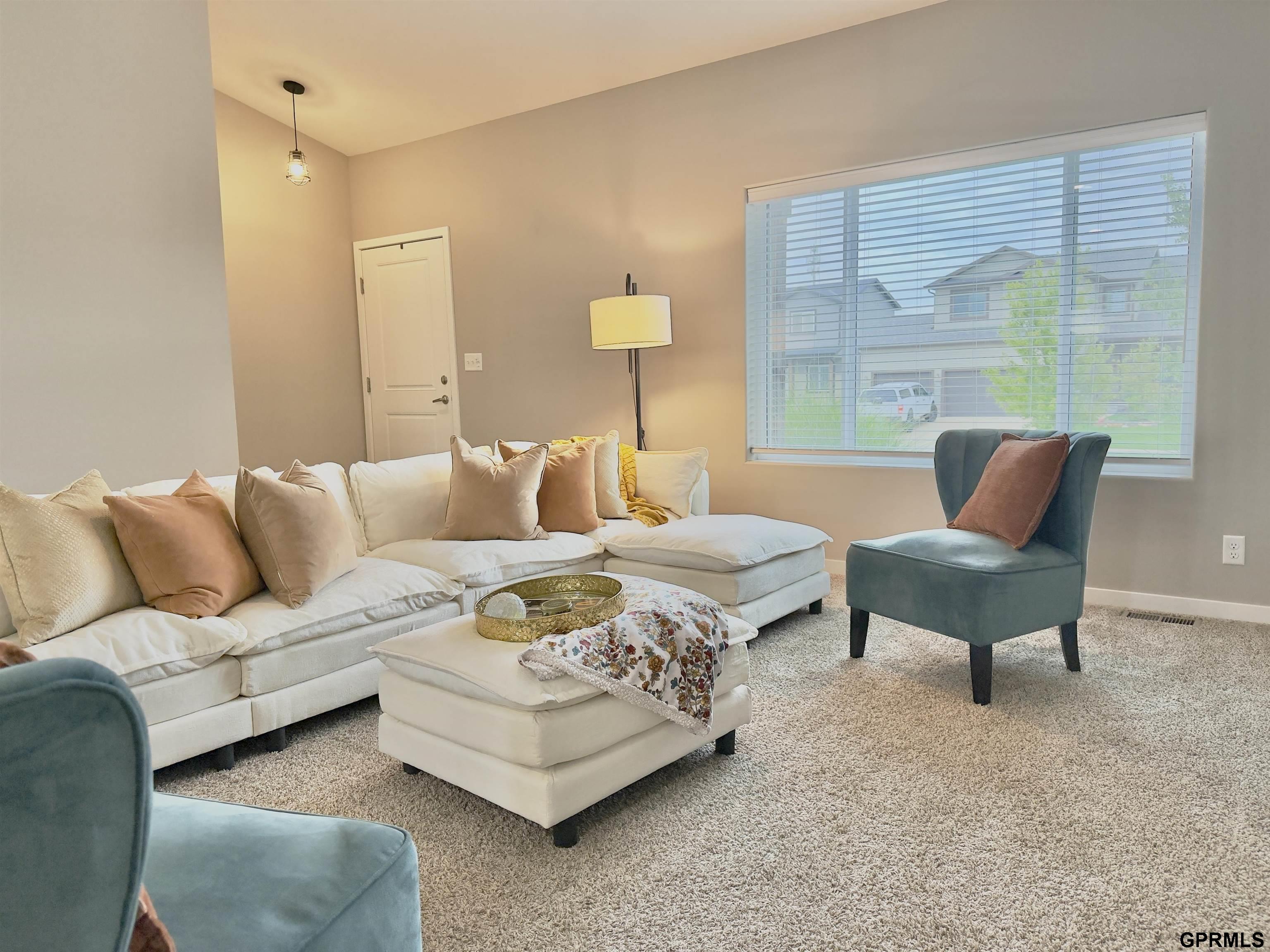 Living room with a cream sectional, ottoman, blue accent chairs, and a large window.