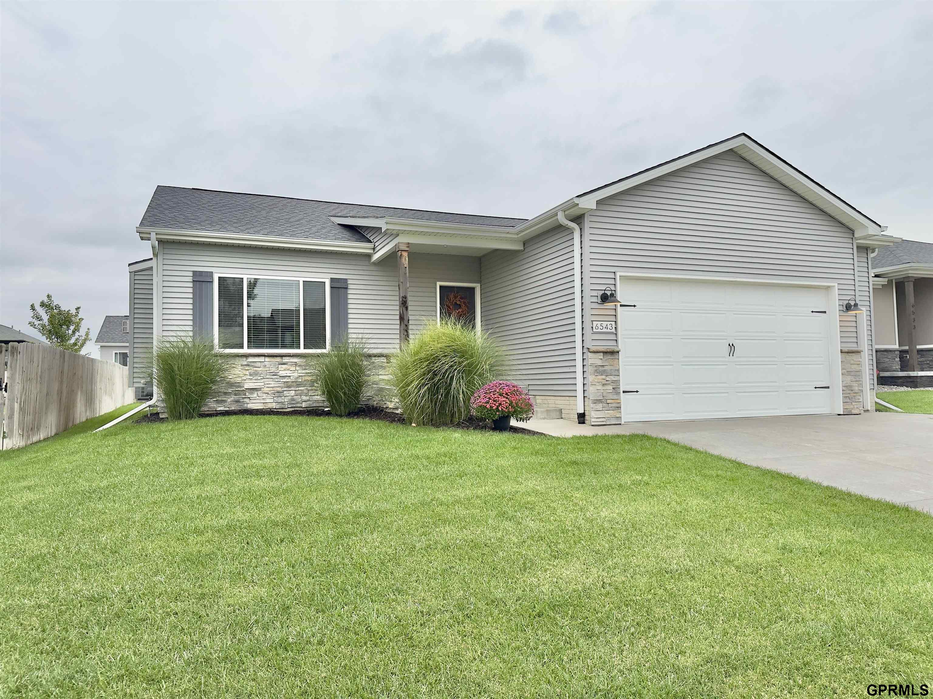Gray-sided house with stone accents, white double garage, landscaped front garden, and broad lawn.