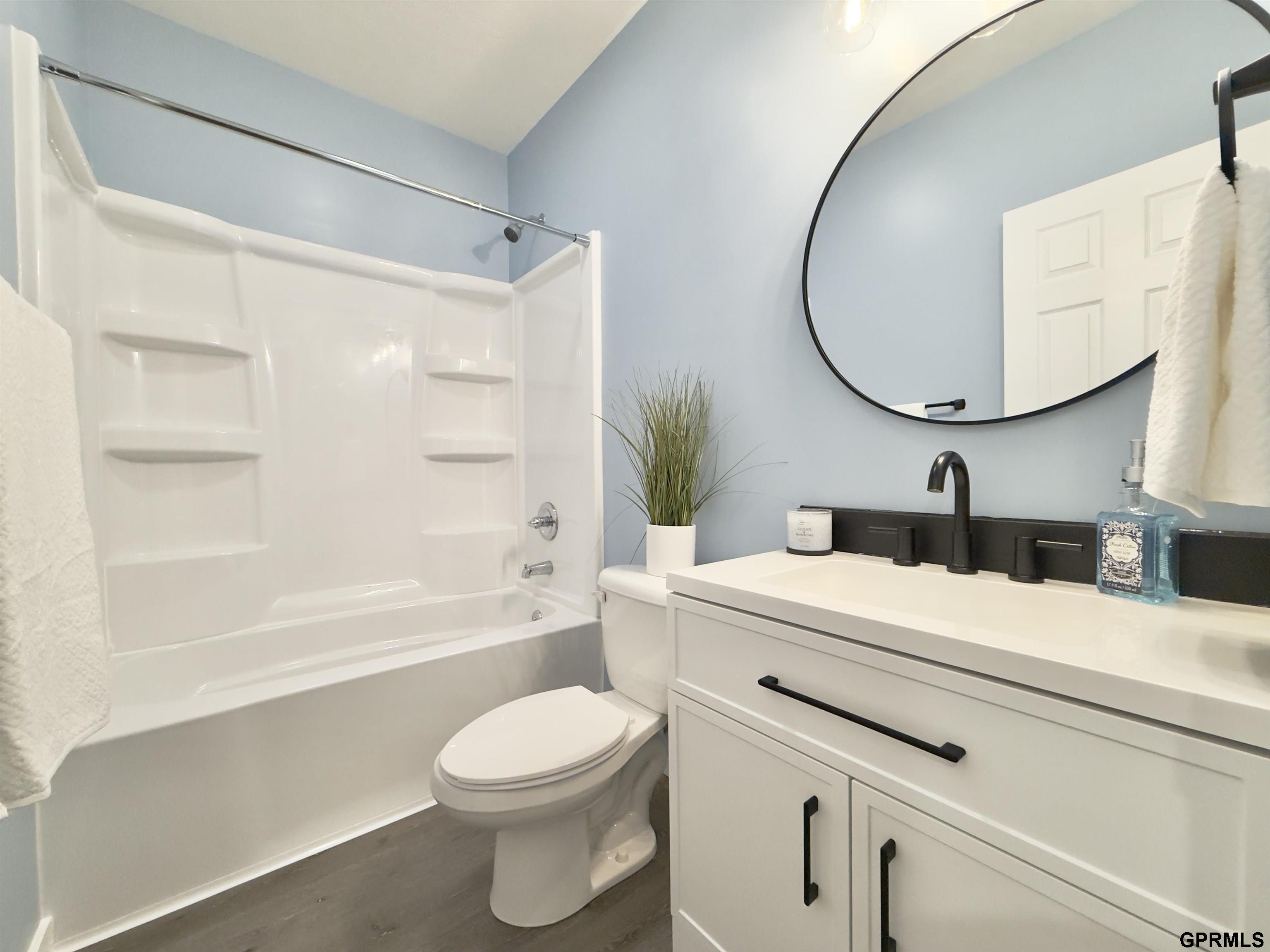 Bathroom with a white tub and shower, toilet, and vanity beneath a large round mirror.
