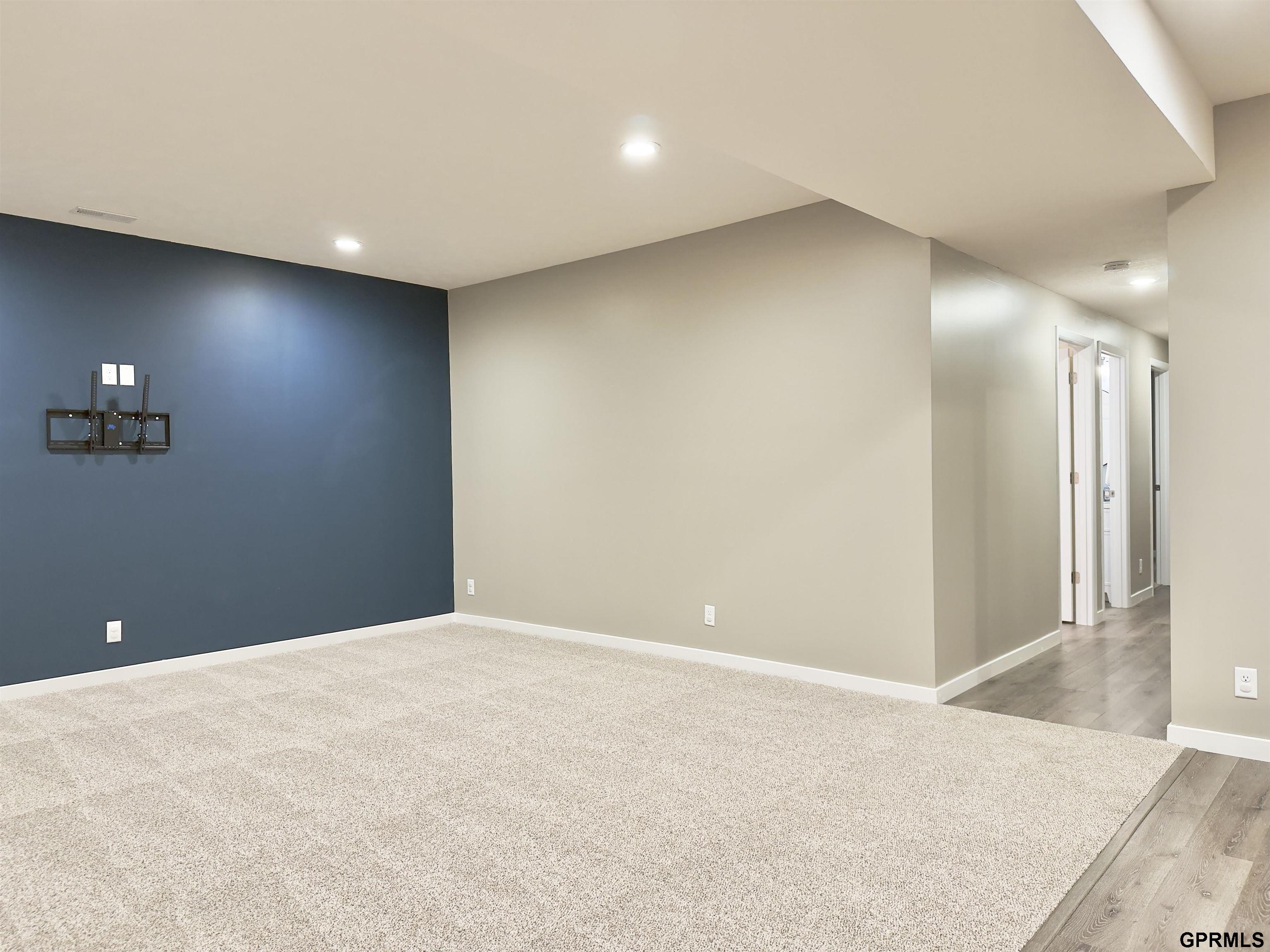 Empty living area with a dark blue accent wall, TV mount, and hallway with wood-look flooring.