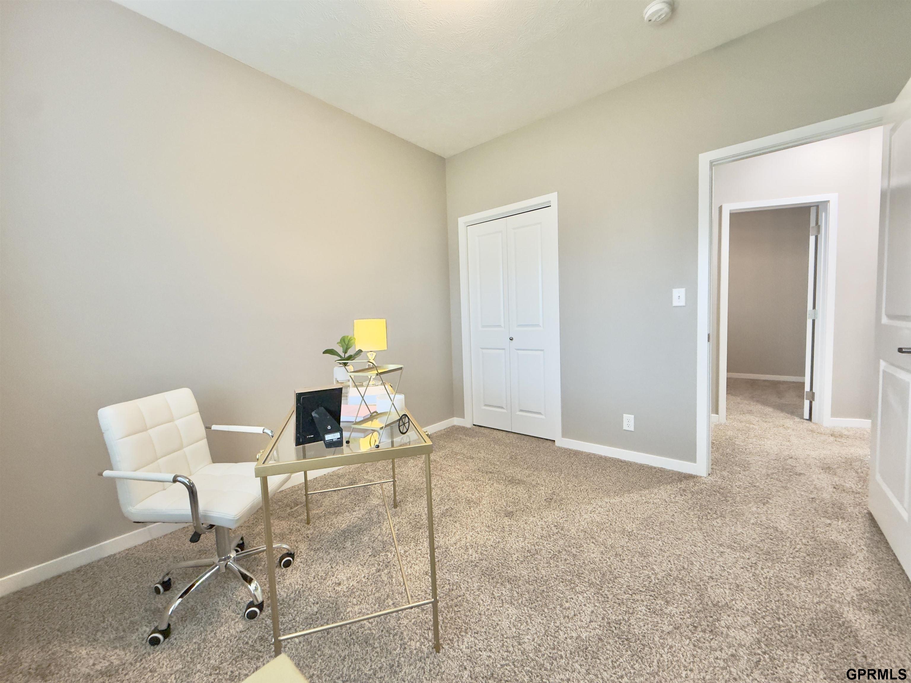 Staged home office with a glass-top desk, white chair, and carpeted floor.